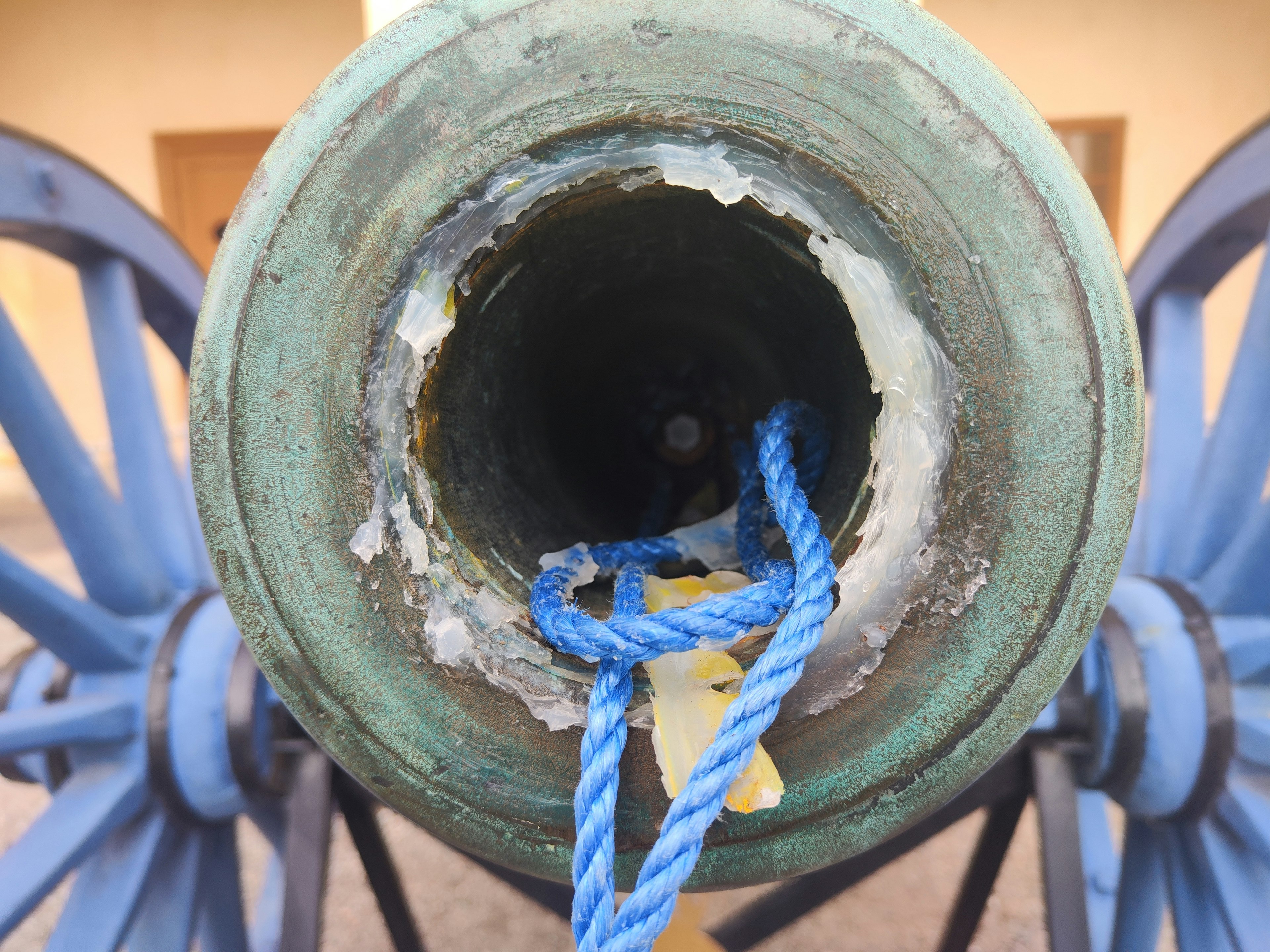 Detalle de un viejo cañón con ruedas azules visto desde la boca