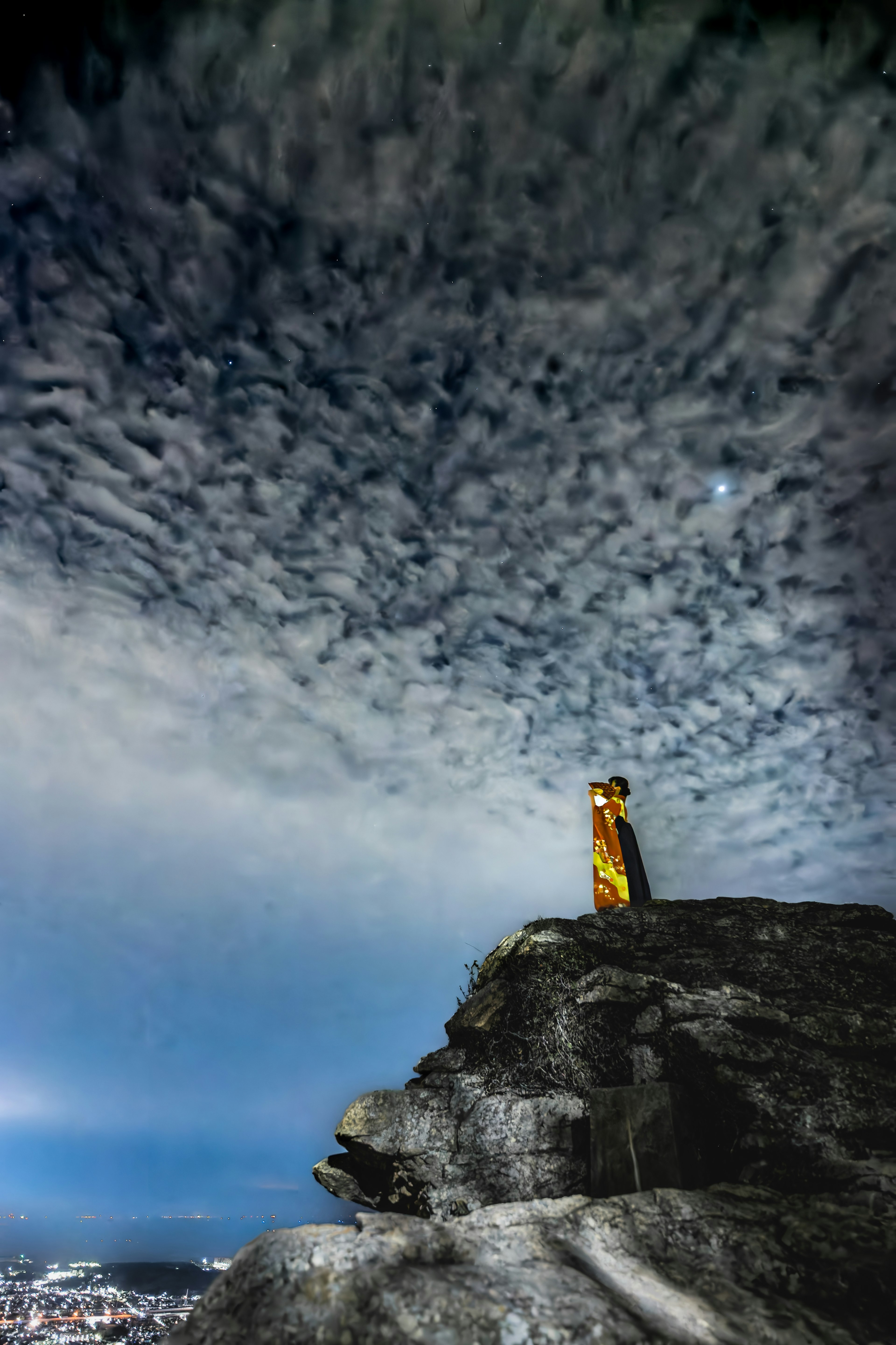 岩の上に立つ黄色い衣装の人物と雲の多い空