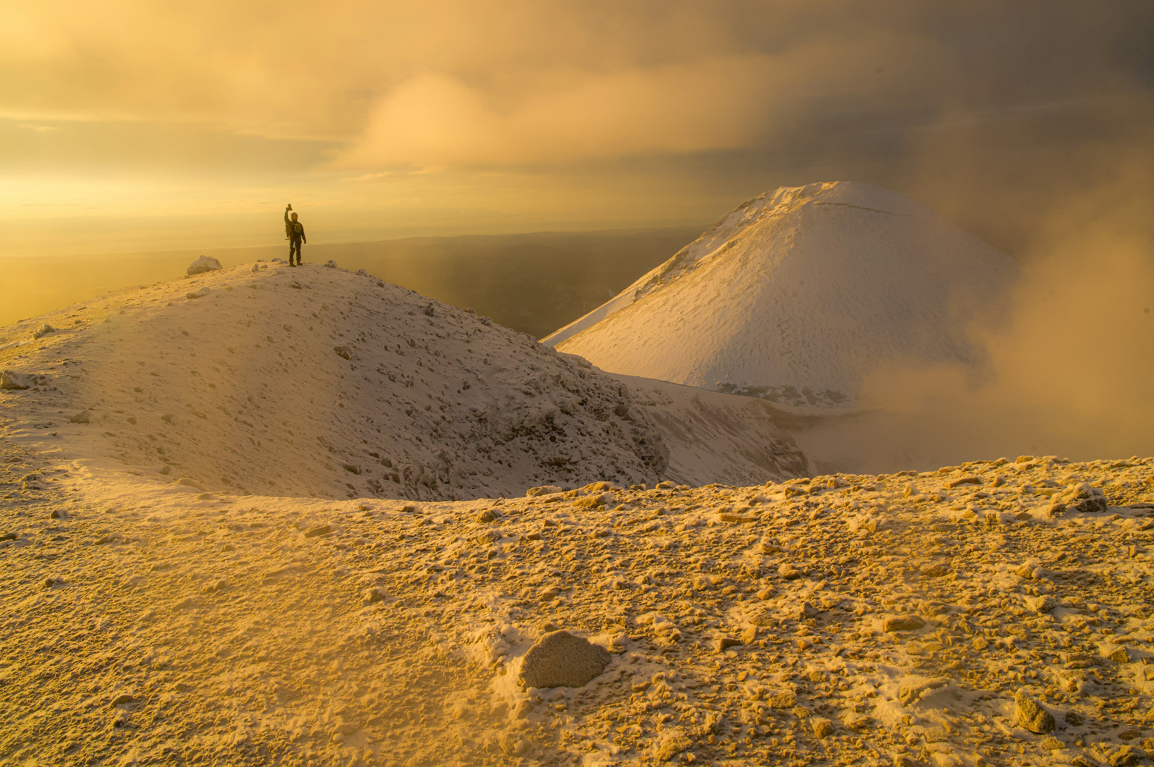 Una persona in piedi su un picco innevato con un paesaggio dorato