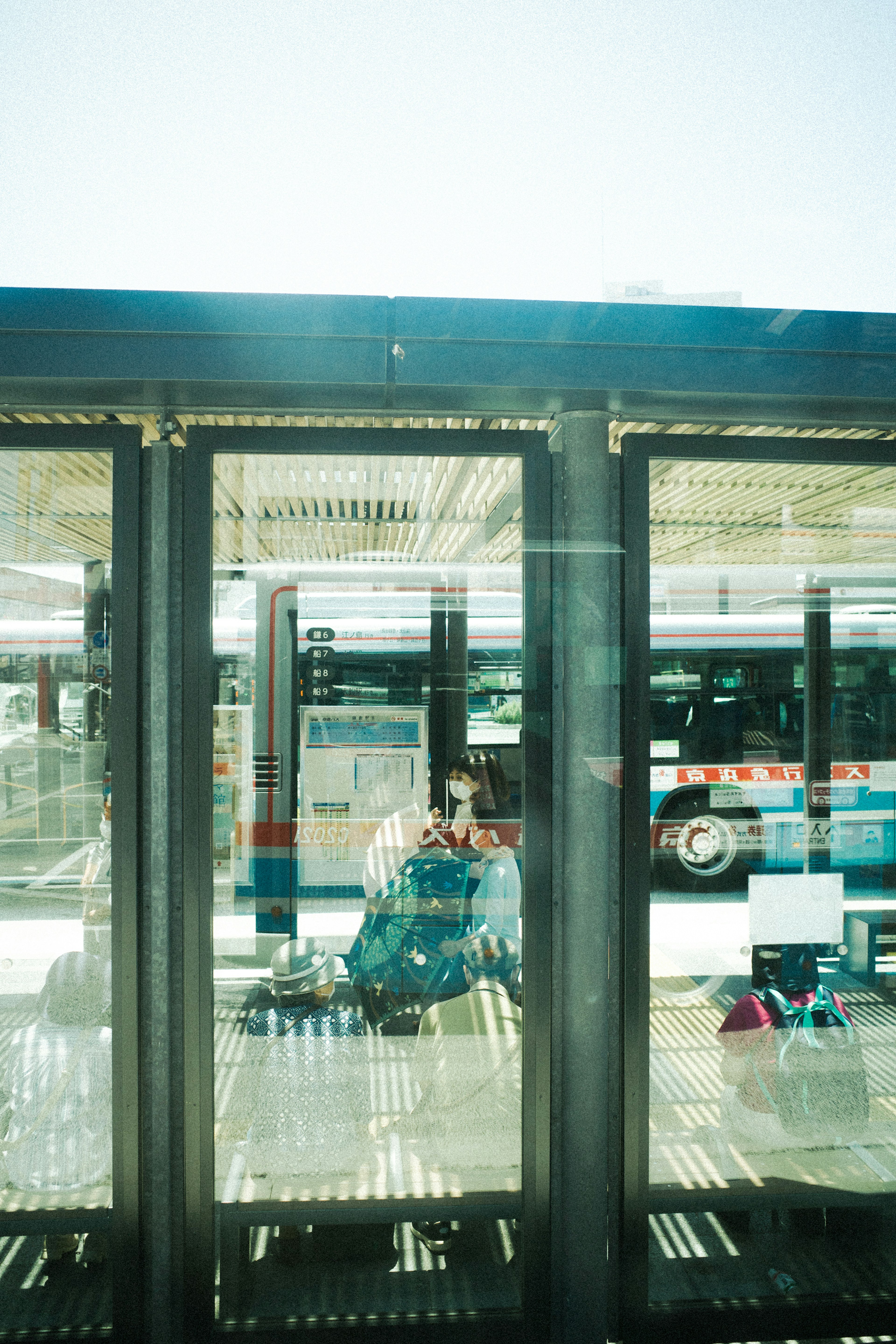 Silhouette orang yang menunggu di halte bus terlihat melalui kaca dengan bus di latar belakang