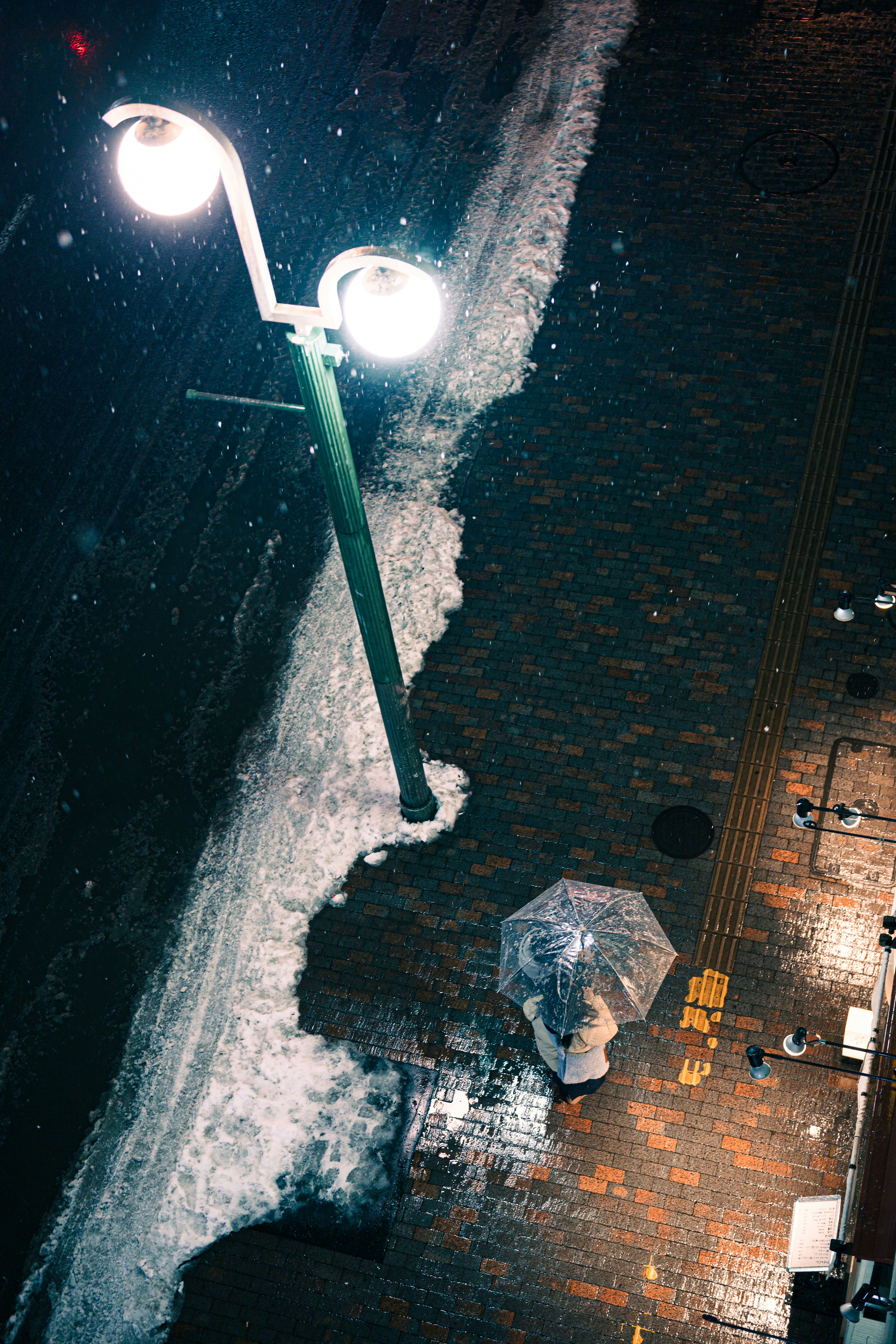 A person with an umbrella on a wet cobblestone street under a streetlight