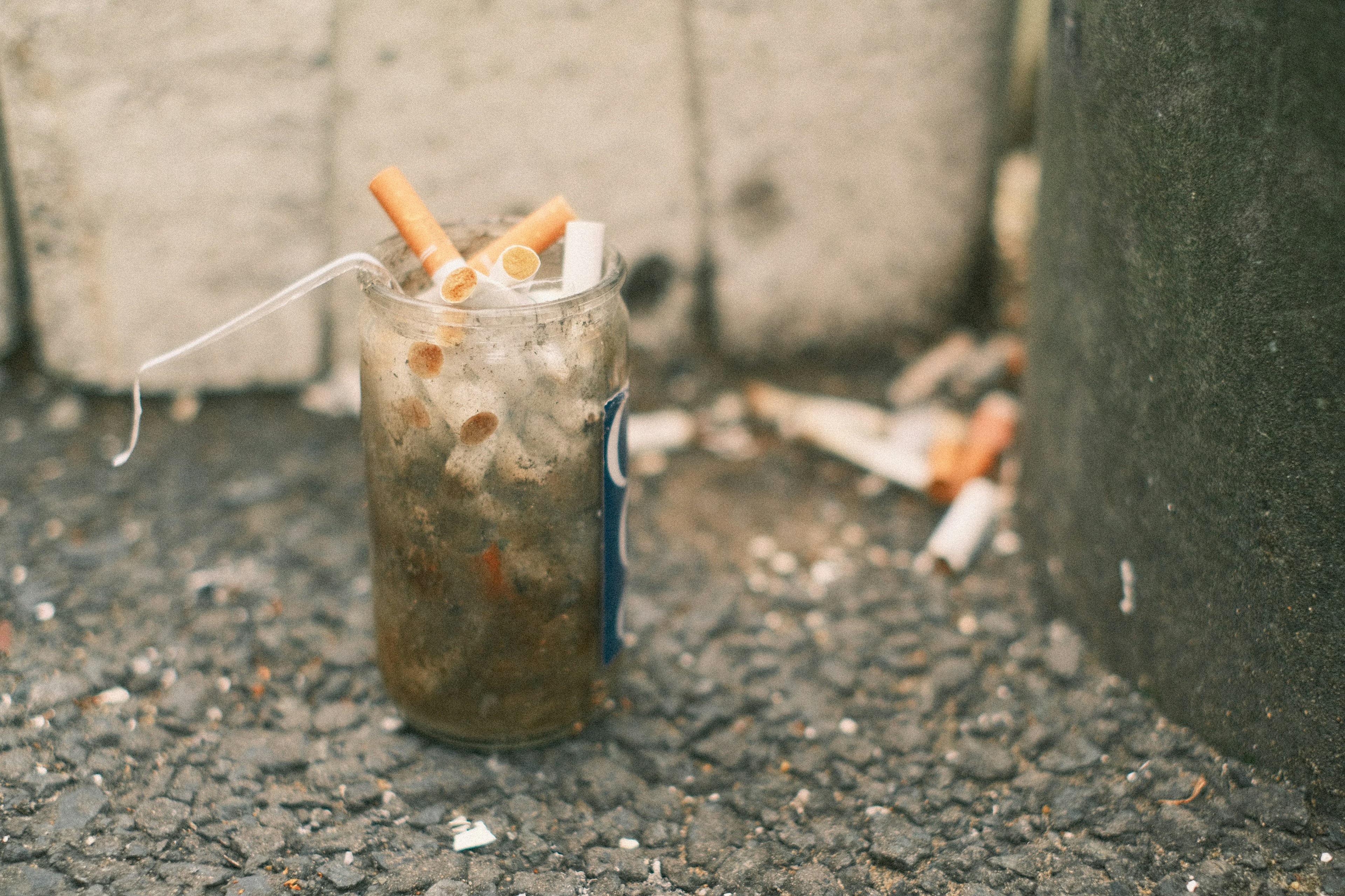 Un verre avec une boisson et des mégots de cigarette posé sur le sol