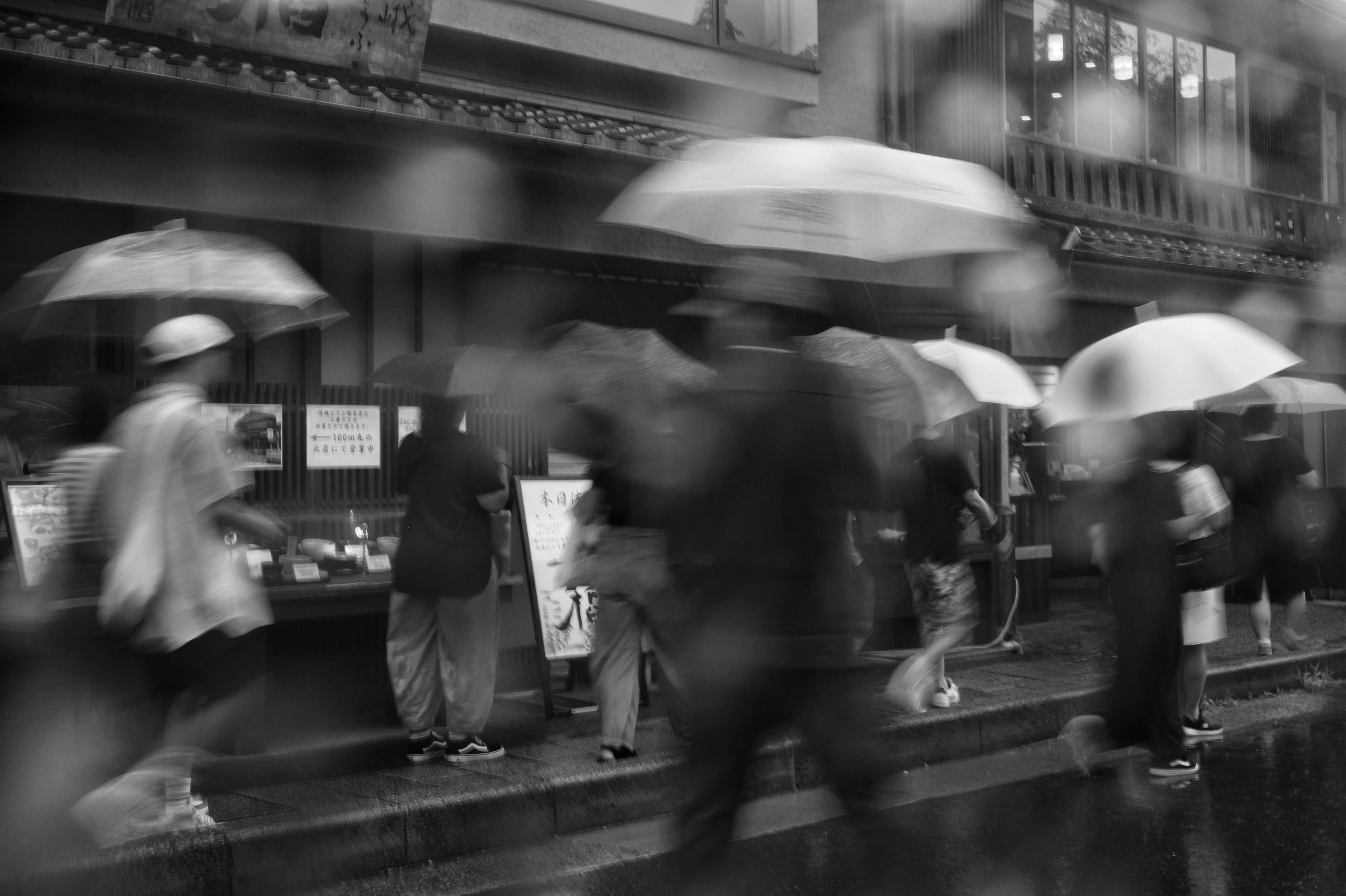 雨の中を歩く人々が傘をさしているモノクロ写真