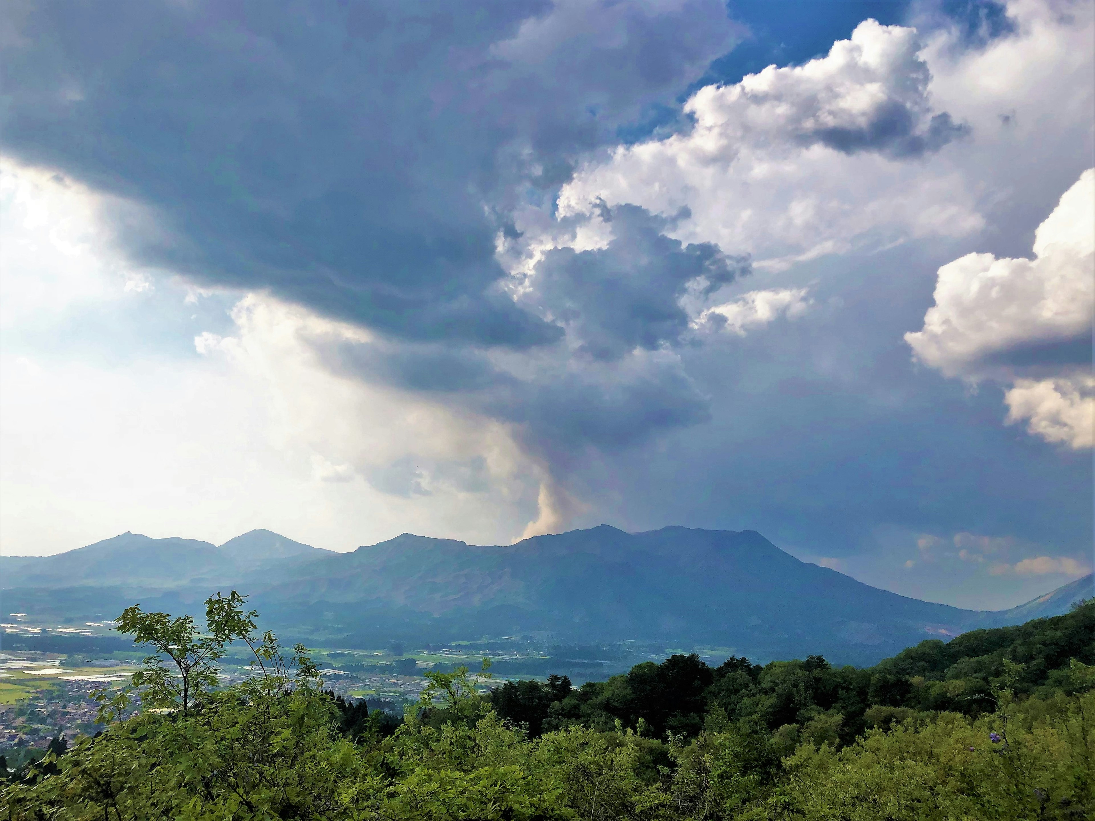 山々と雲の中から噴煙を上げる火山の景色