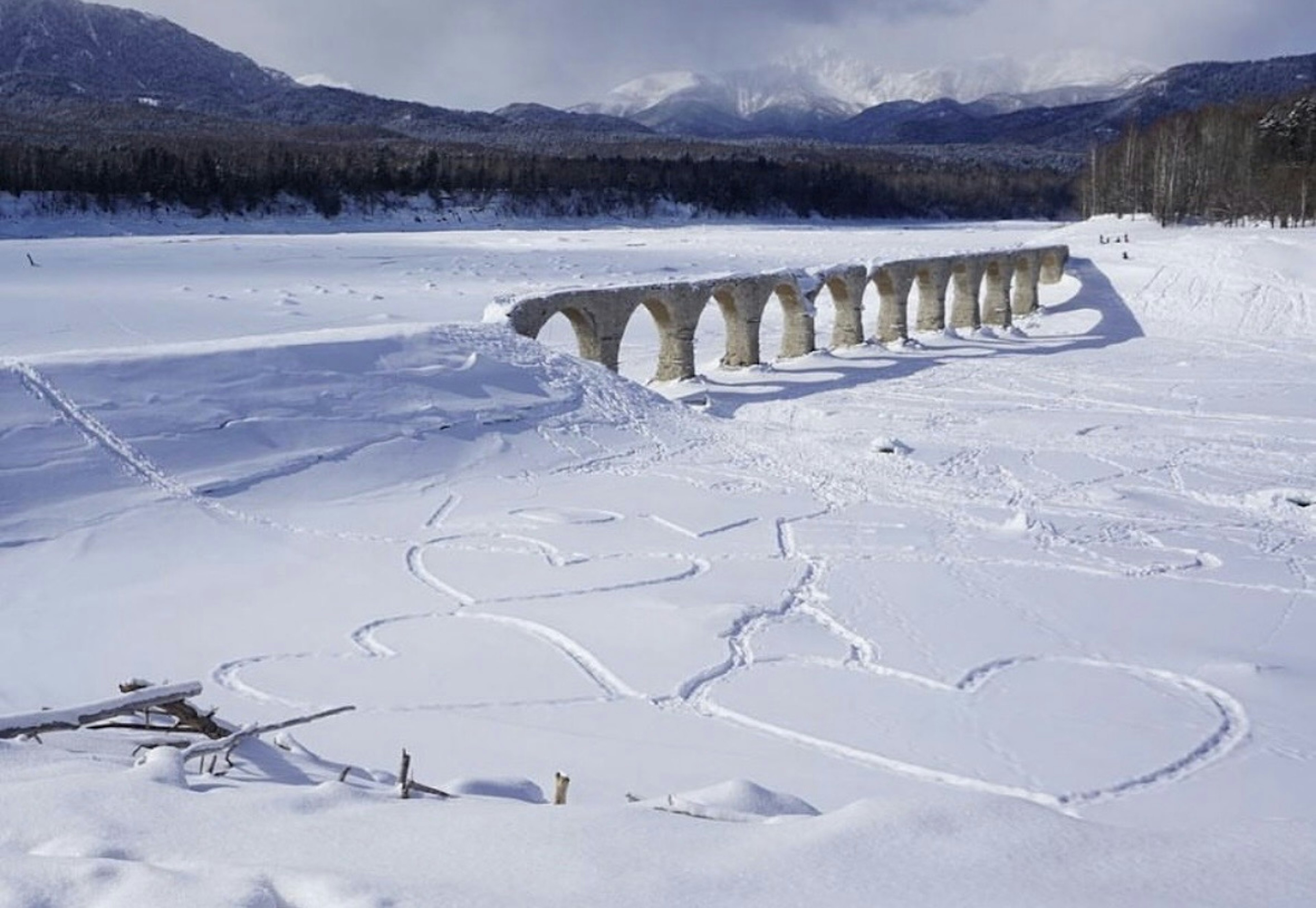 A snowy landscape featuring a river and an arch bridge structure