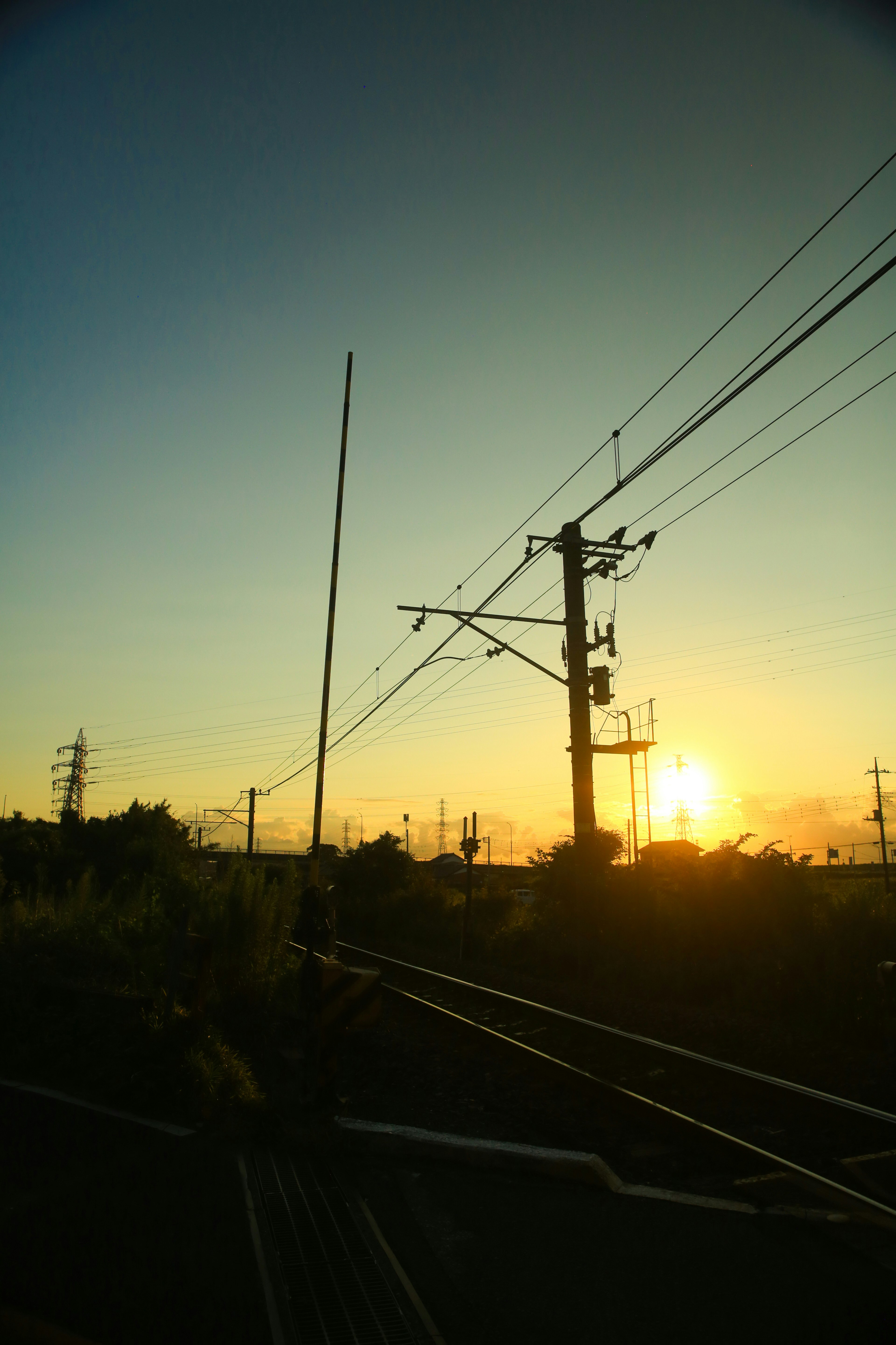 Siluet saluran listrik kereta api dan tiang utilitas di latar belakang langit matahari terbenam