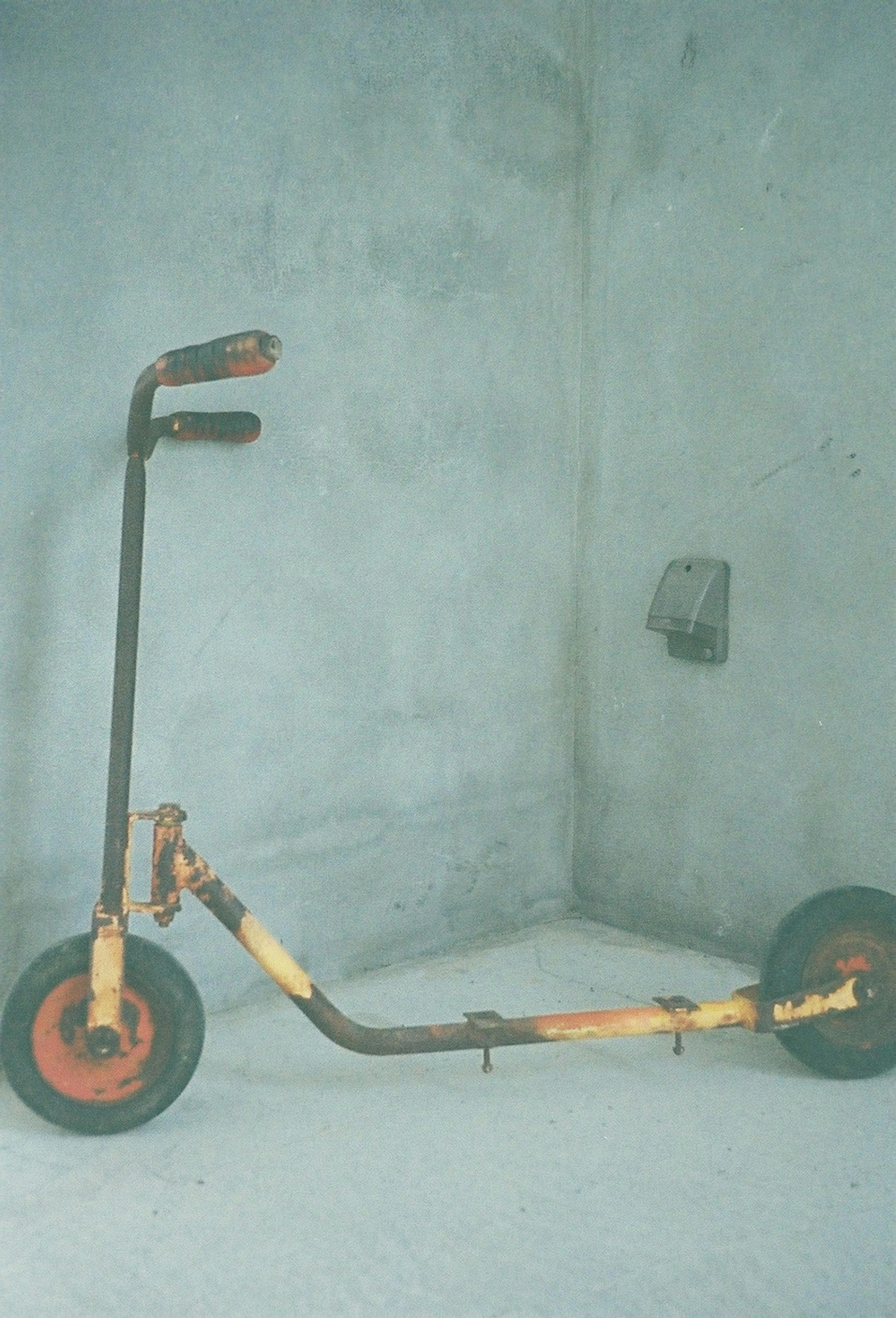 Rusty scooter leaning against a gray wall in a corner