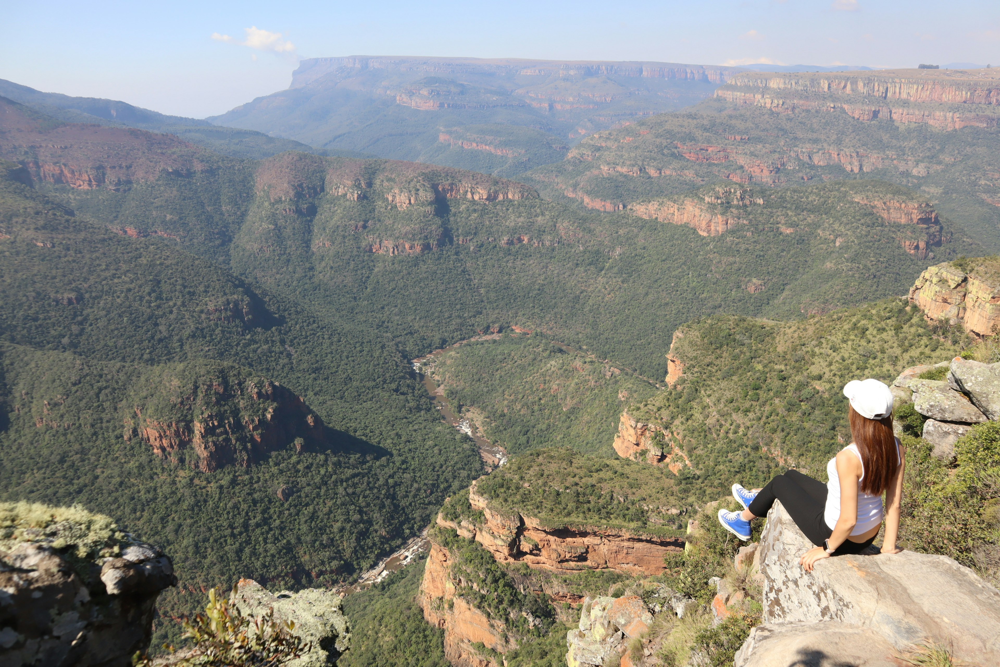 Una mujer sentada en una roca con vista a un vasto cañón y un paisaje montañoso