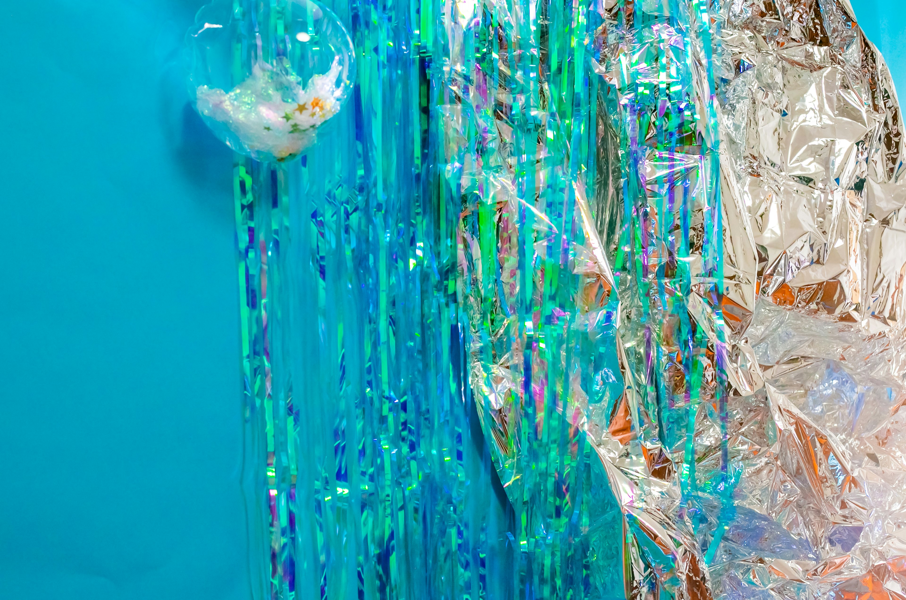 Shiny silver material and iridescent strips hanging against a blue background