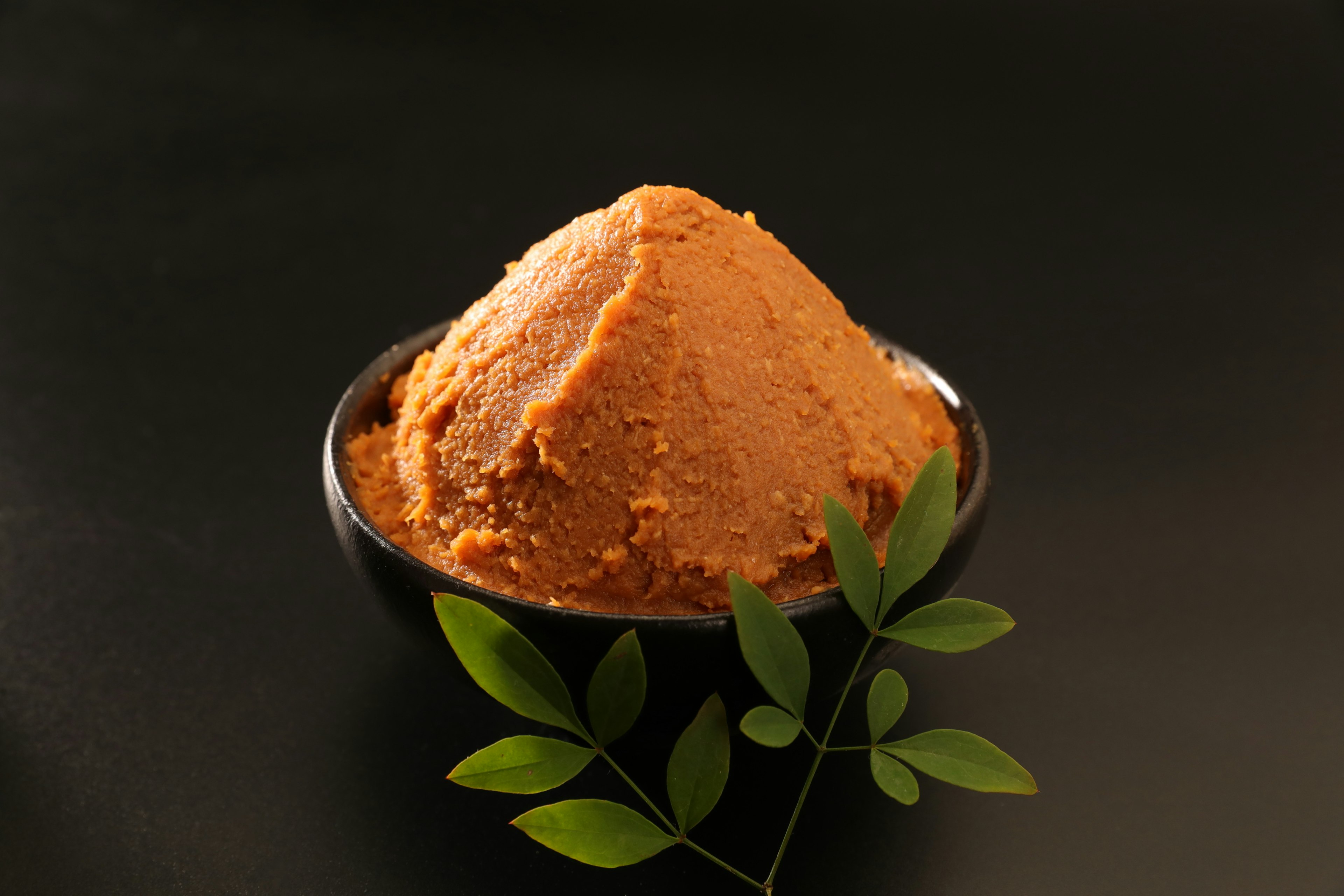 Red miso piled in a black bowl with green leaves