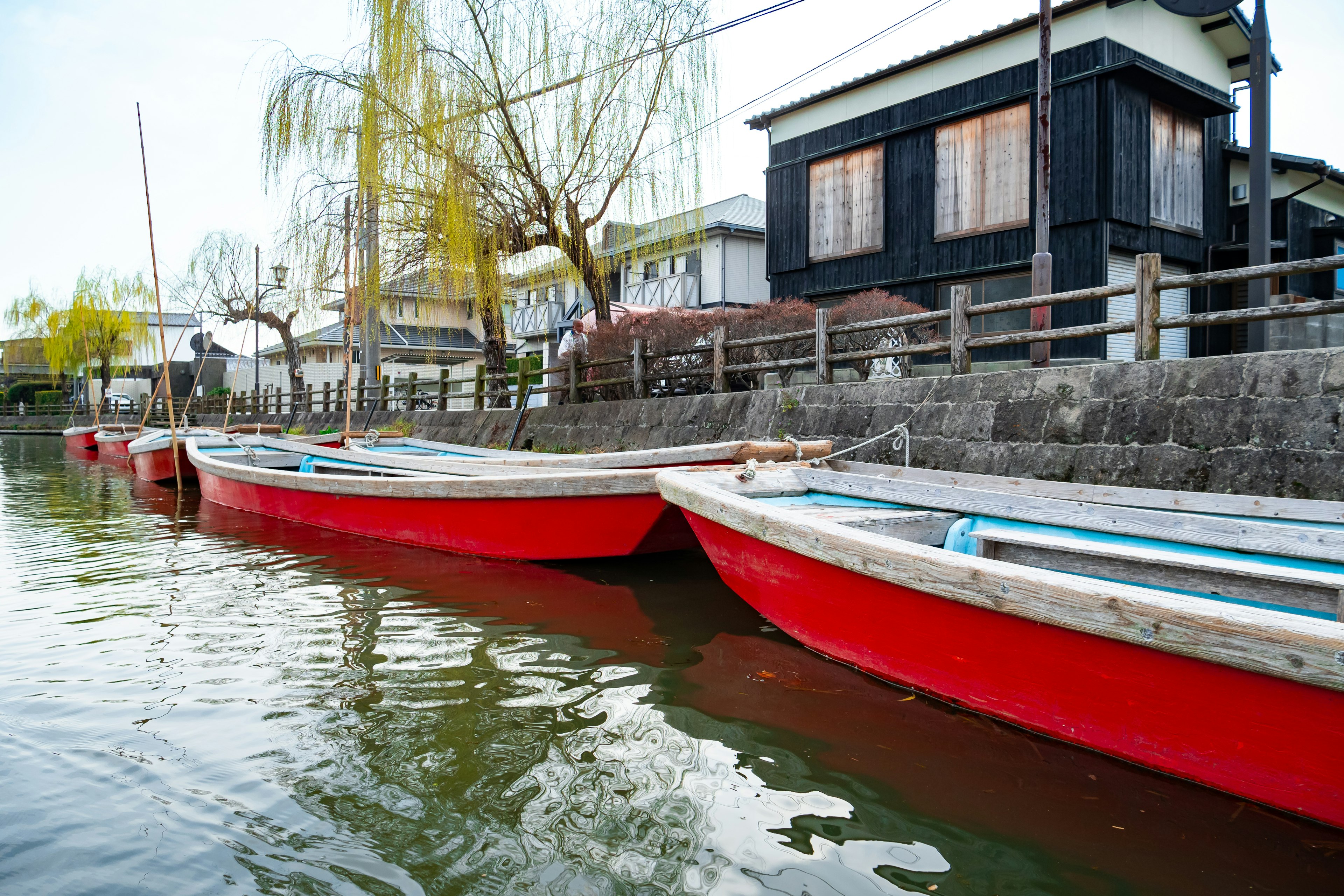 Perahu merah mengapung di air dengan rumah hitam di latar belakang