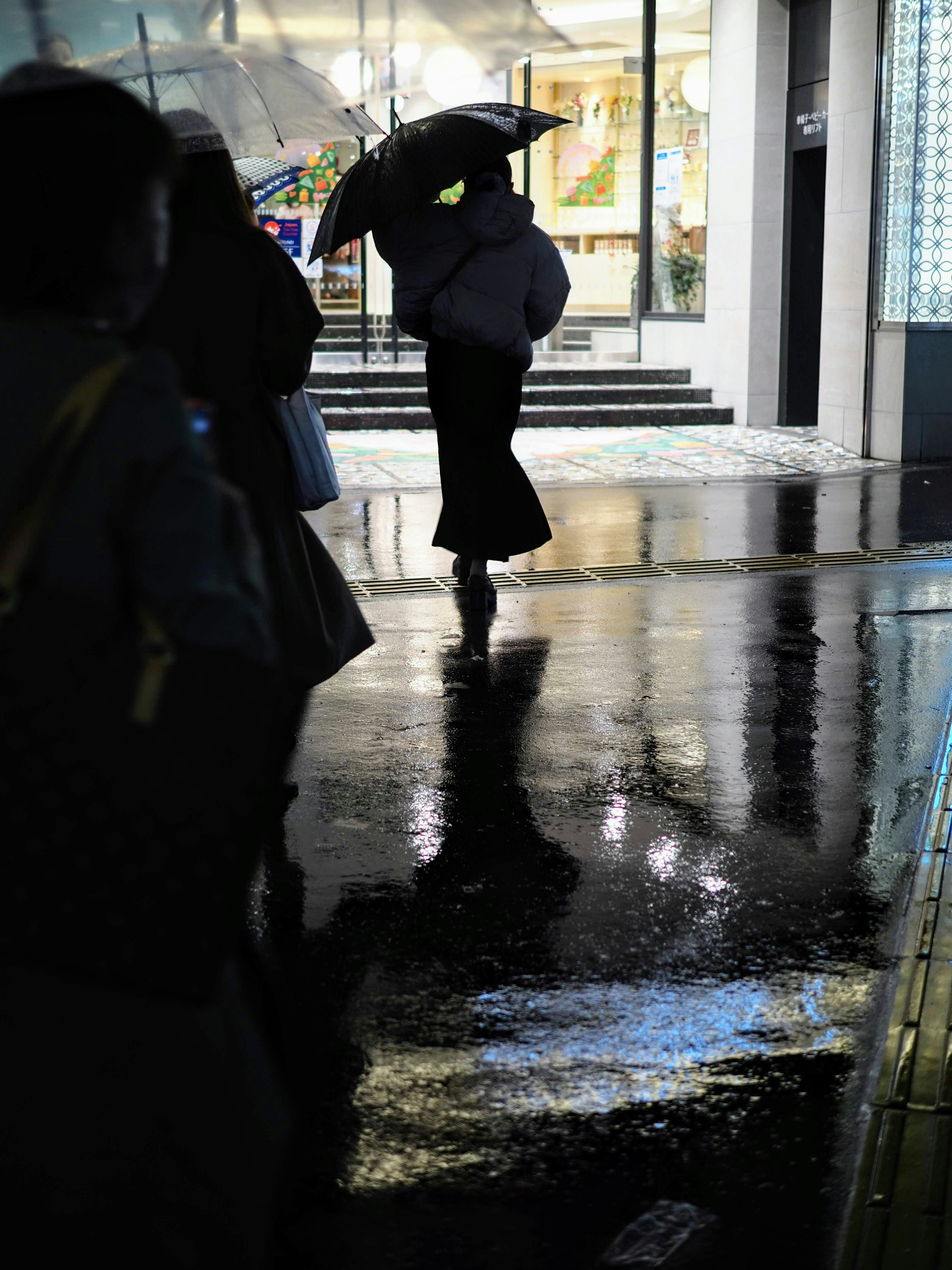 傘を持って歩く人のシルエットが映る雨の街並み