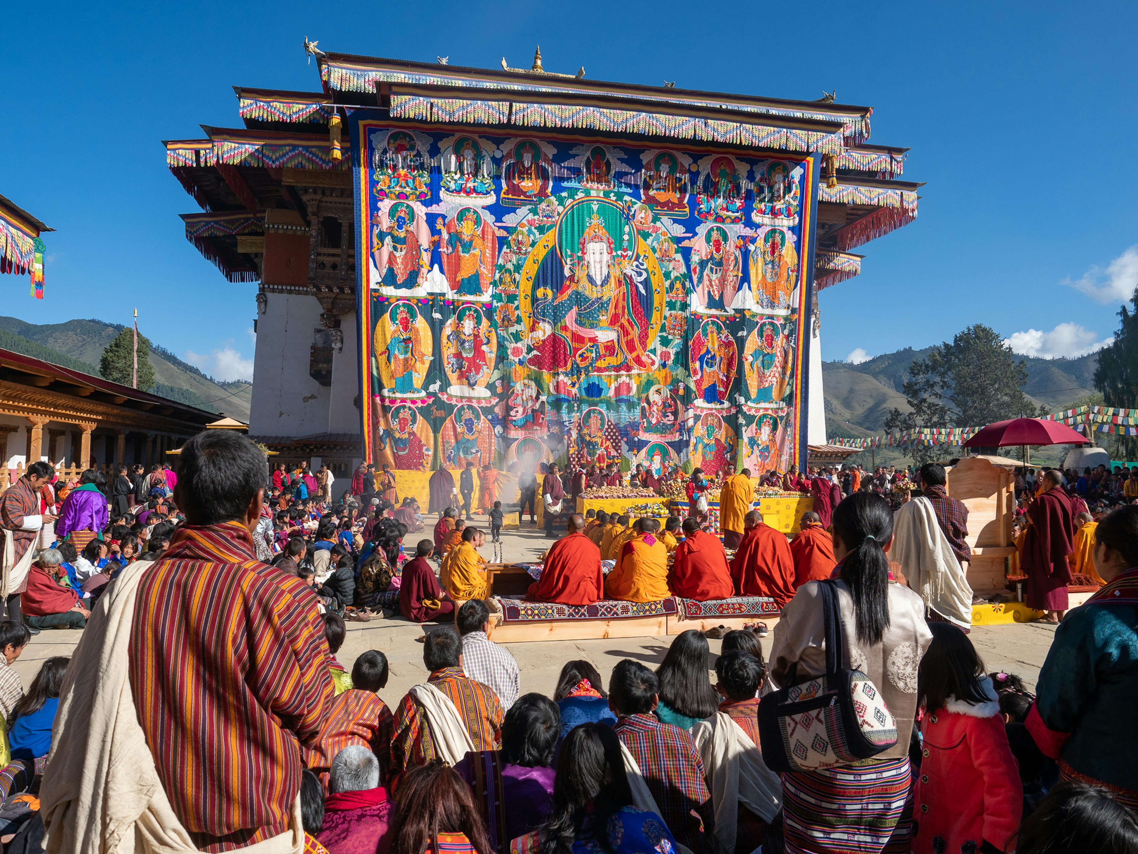 Monaci buddisti che eseguono rituali davanti a un grande thangka durante un festival in Bhutan