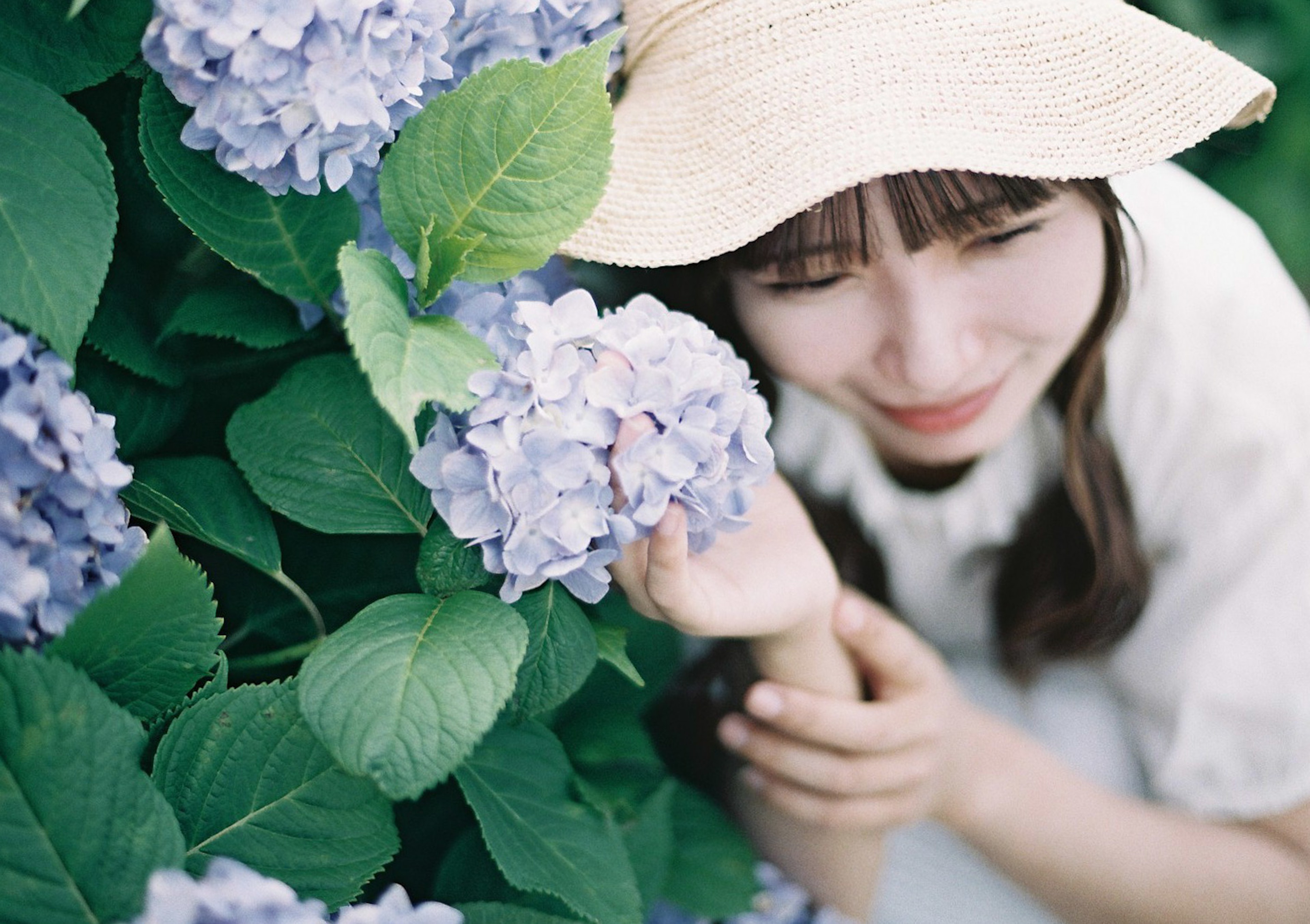 Mujer sonriendo cerca de flores de hortensia con un sombrero de paja