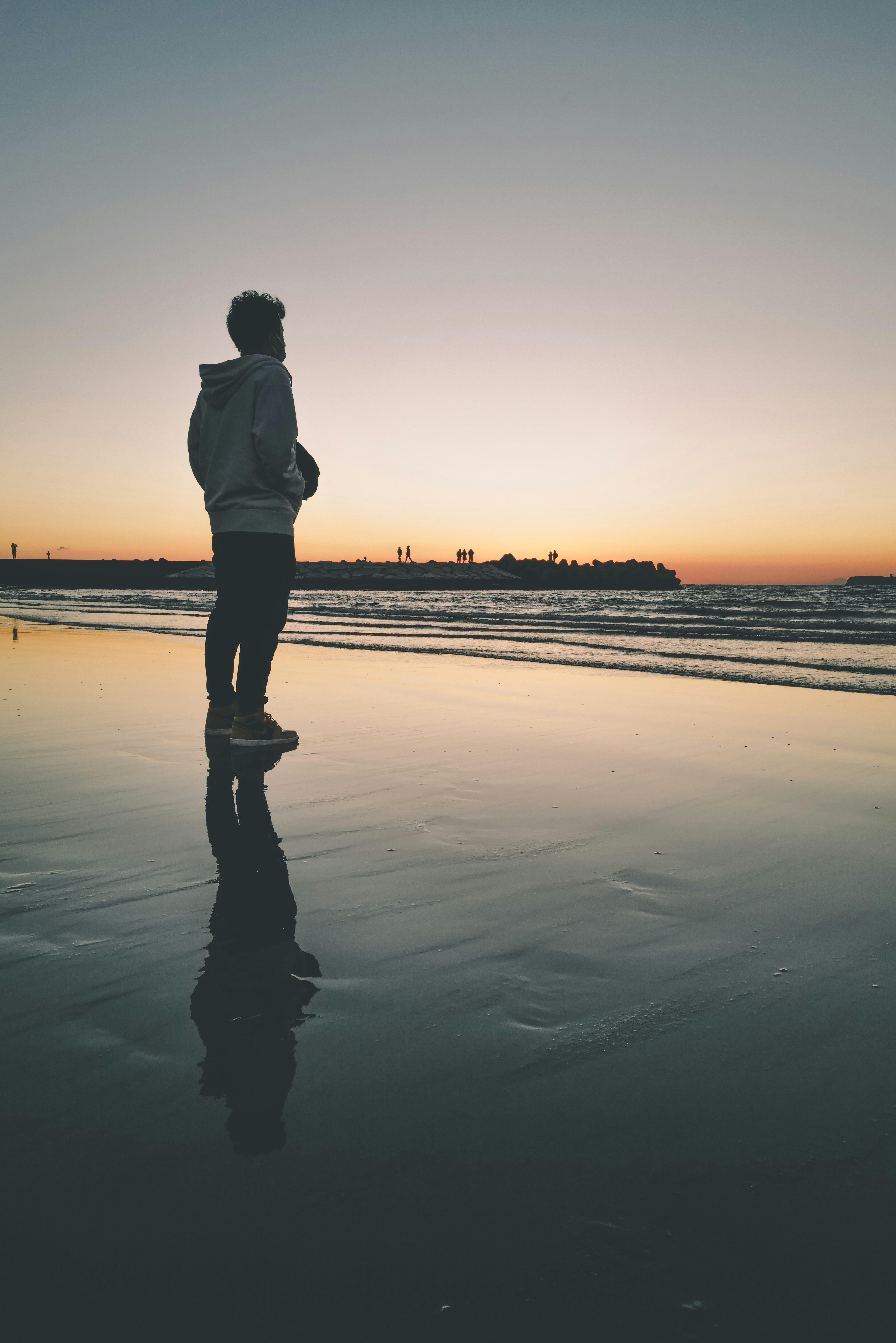 Silhouette of a person standing on the beach at sunset with reflection in the water