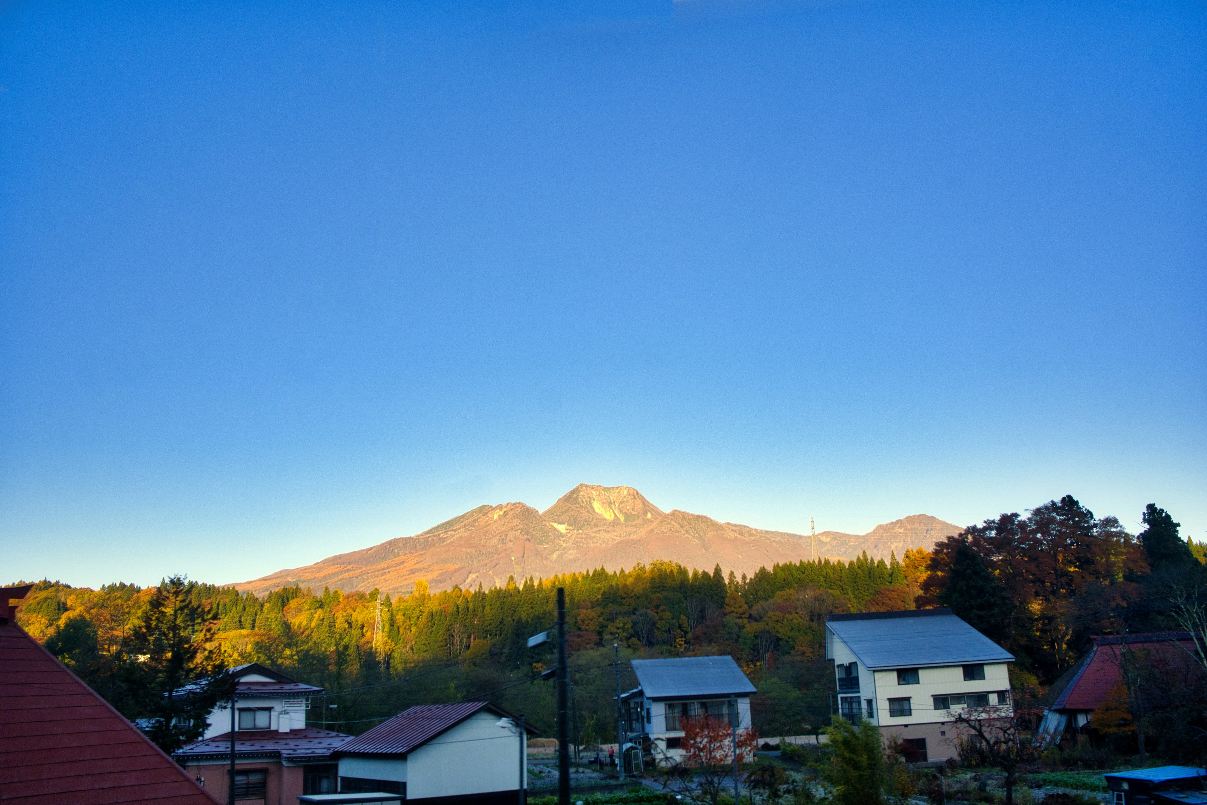 Pemandangan desa yang tenang dengan langit biru dan pegunungan di latar belakang