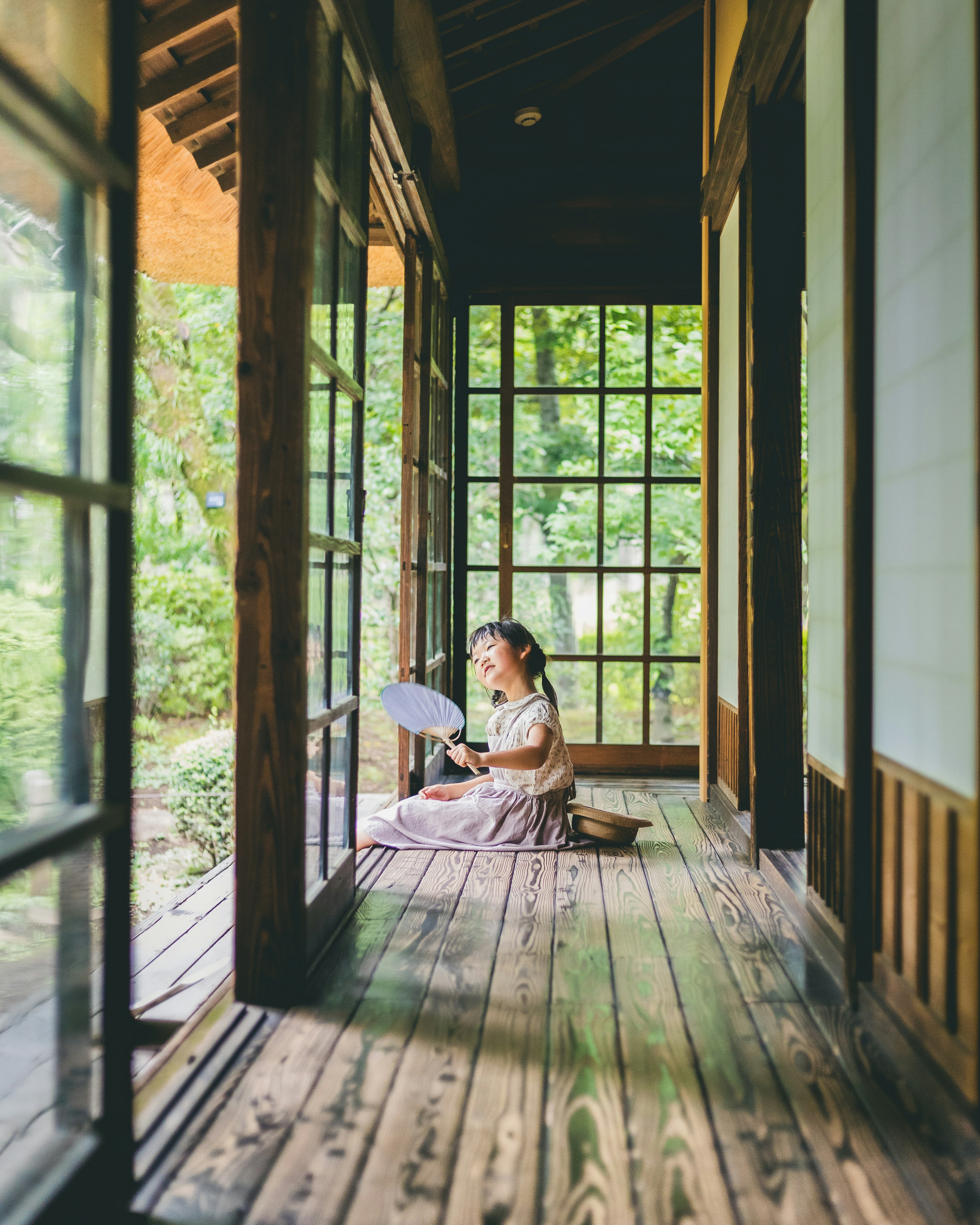 Seorang gadis memegang kipas di koridor Jepang tradisional yang dipenuhi cahaya alami