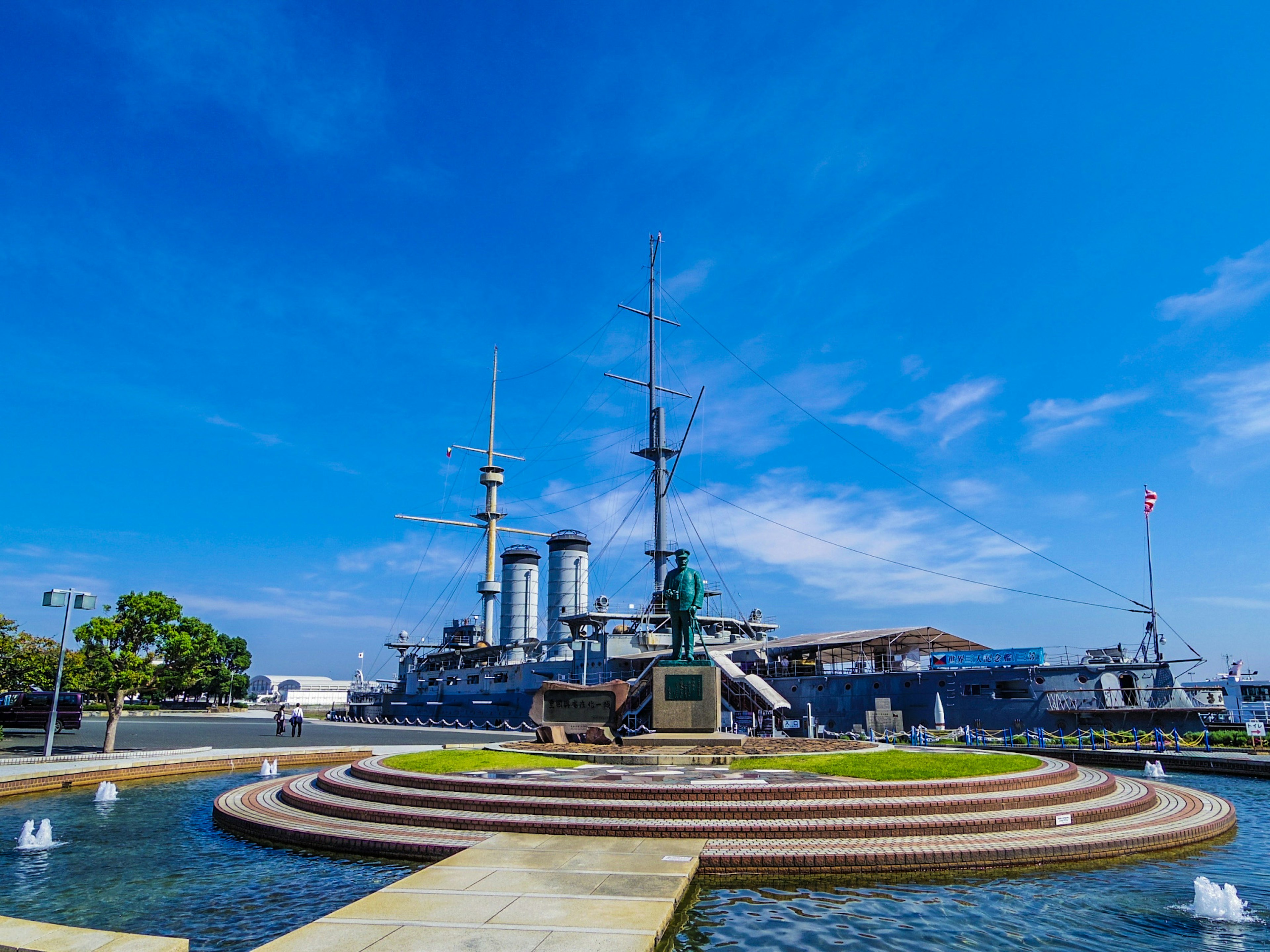 青い空の下にある戦艦と噴水のある公園の風景