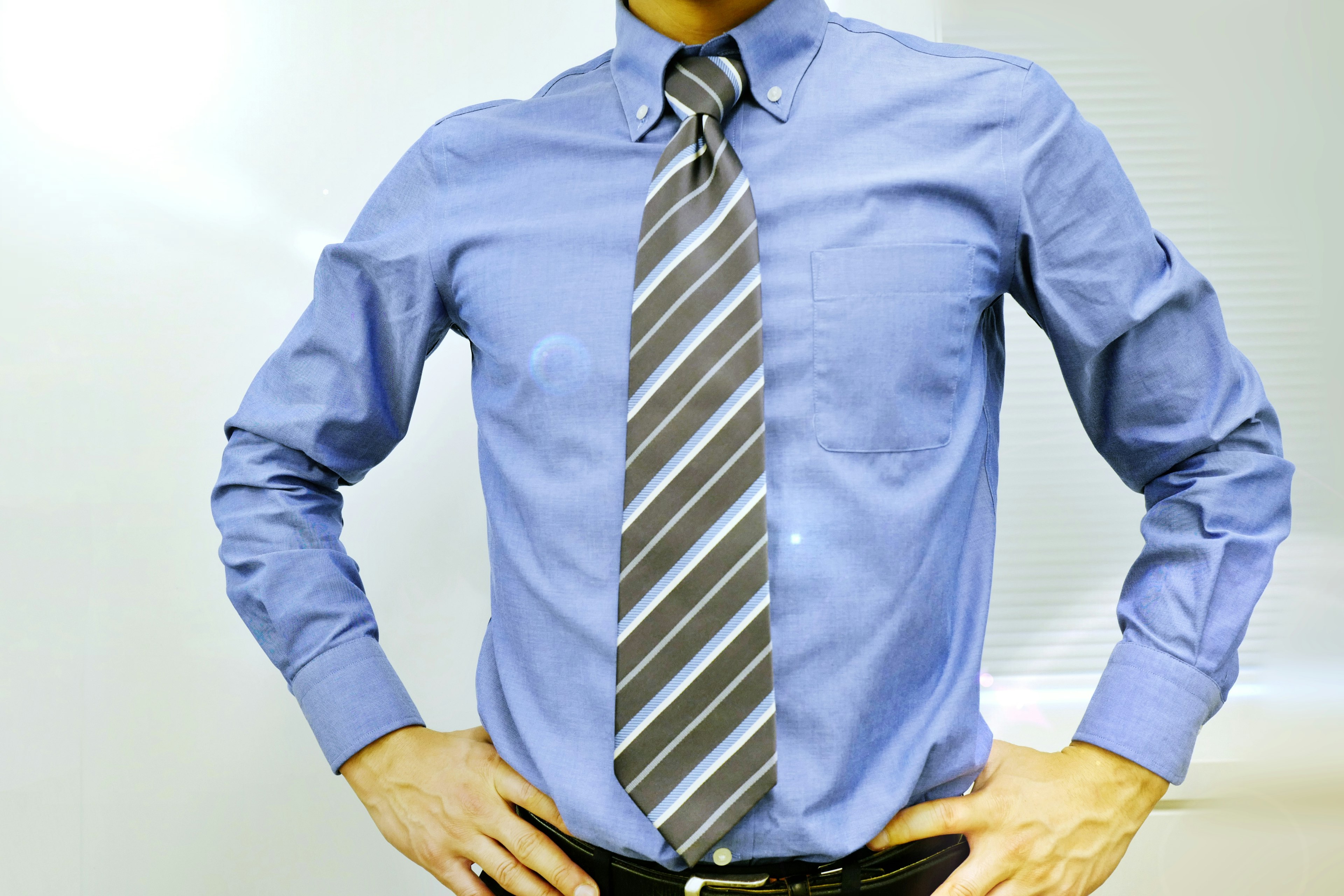 Homme portant une chemise bleue et une cravate rayée avec les mains sur les hanches