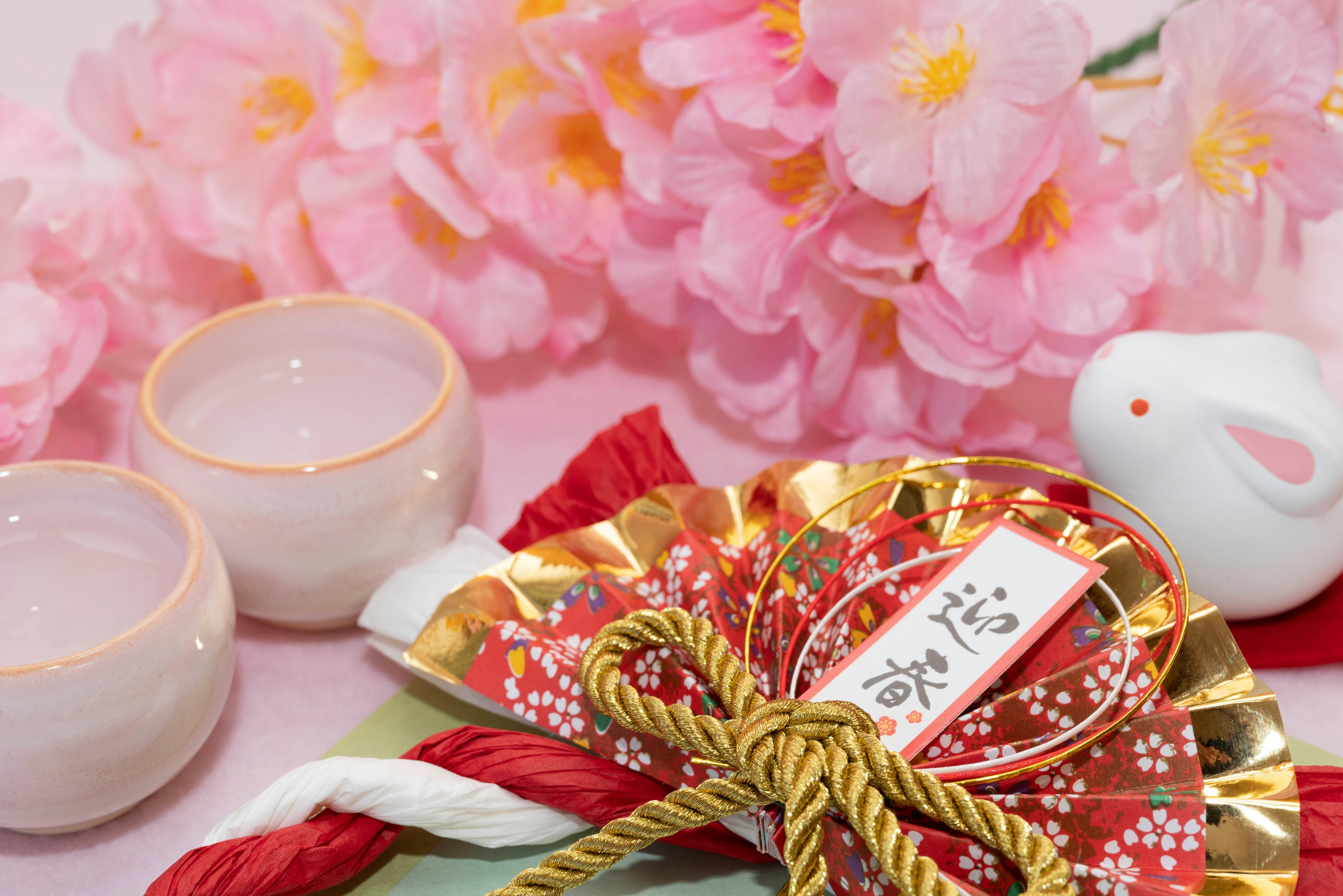 Elementos tradicionales japoneses con una figura de conejo blanco y flores rosas de fondo