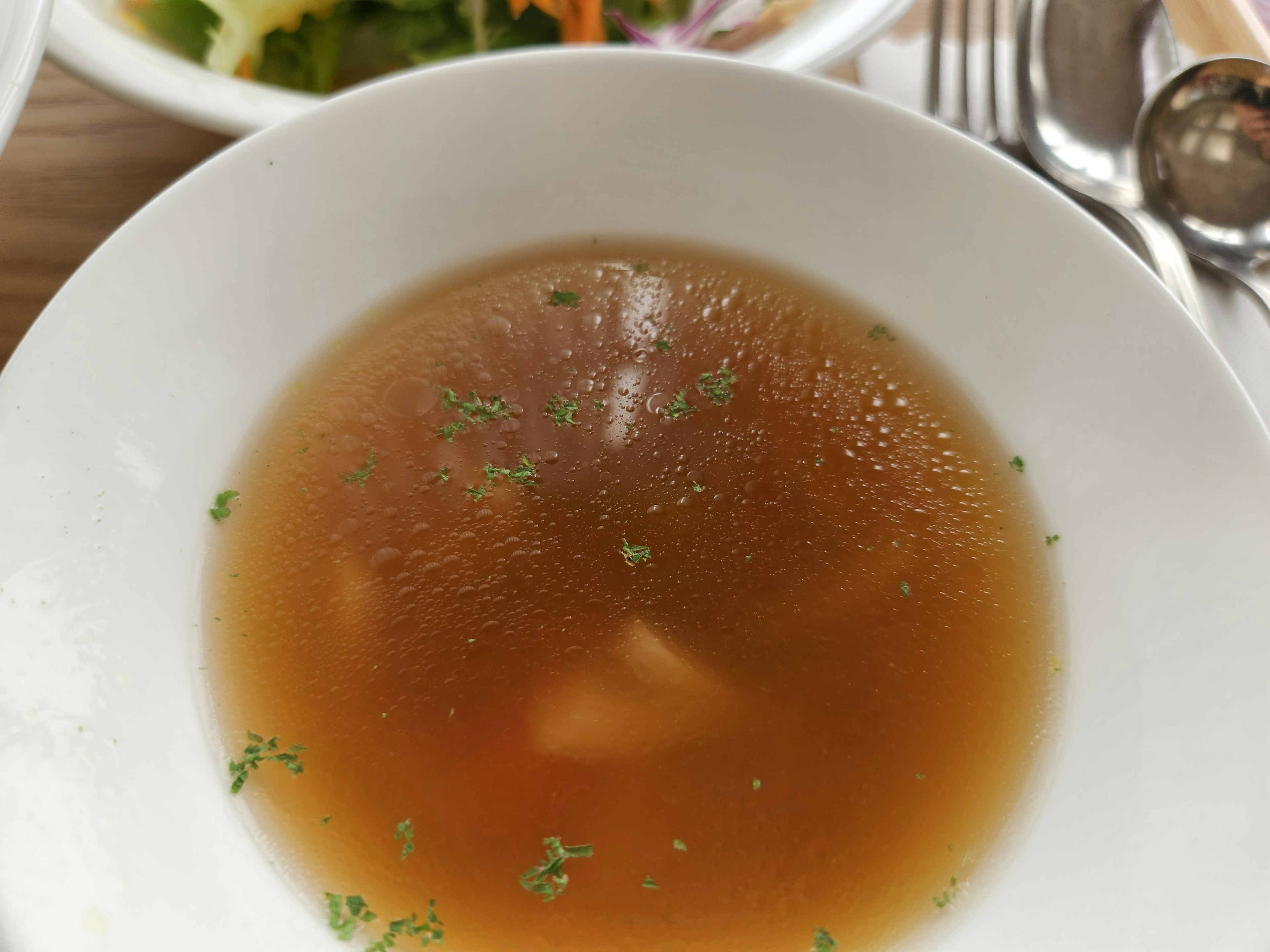 Brodo chiaro in una ciotola bianca con piccole guarnizioni di erbe