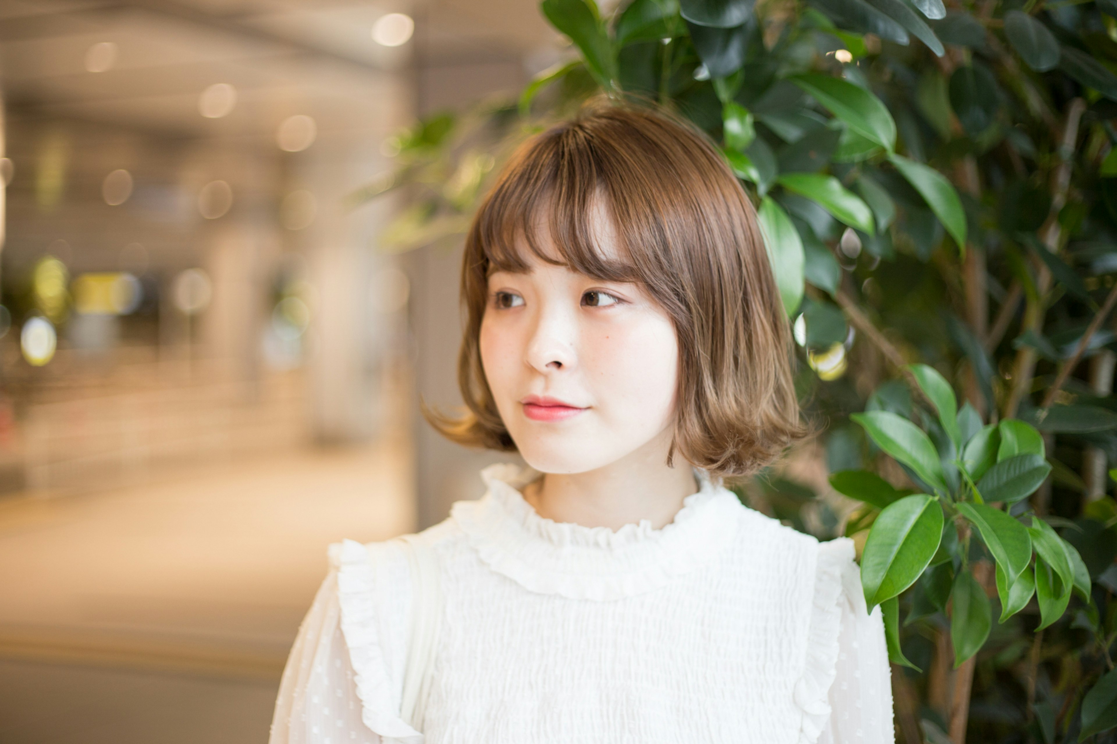 A woman in a white blouse standing in front of a plant