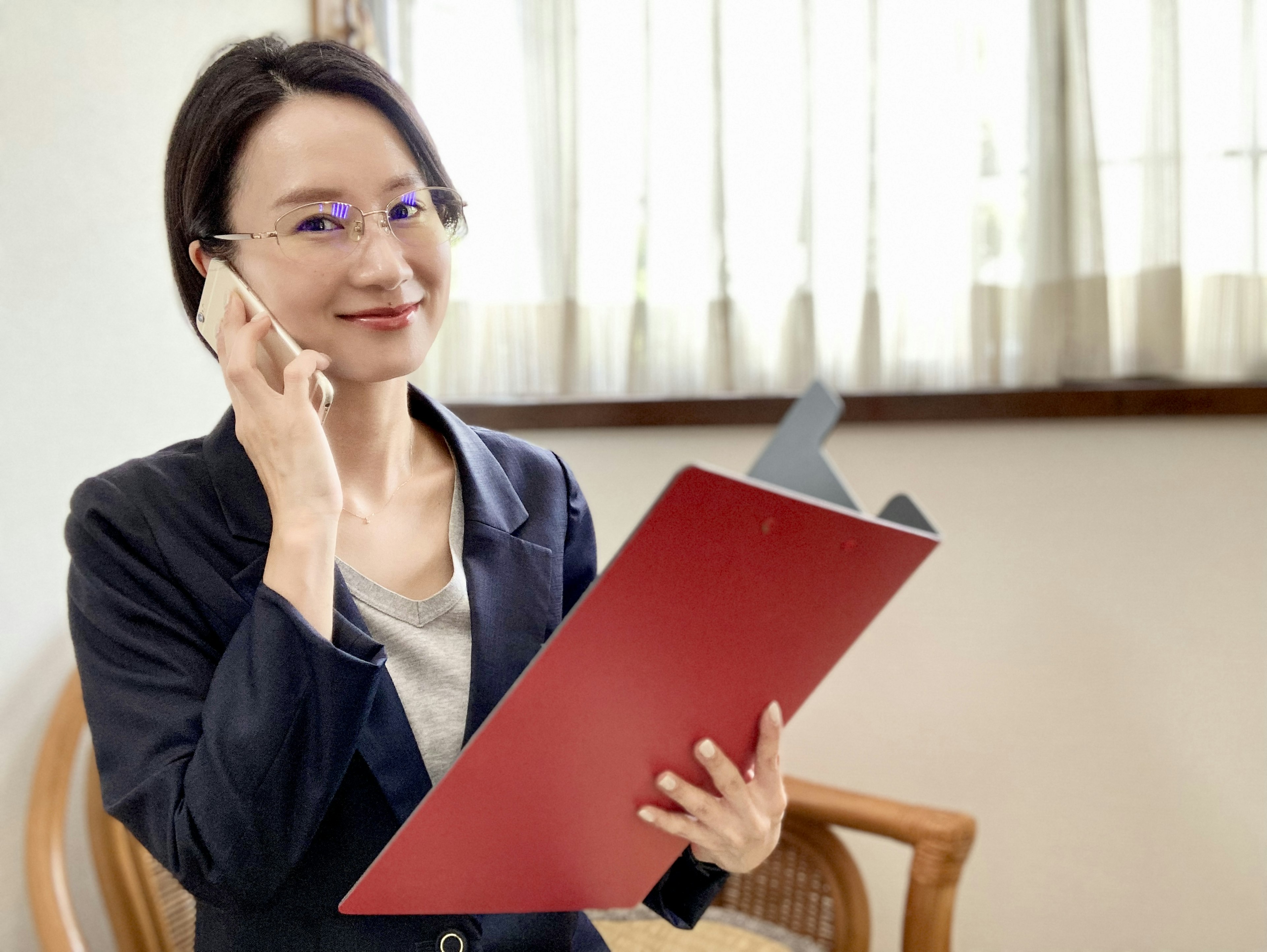 Donna in abito da lavoro che tiene un cartella rossa mentre parla al telefono