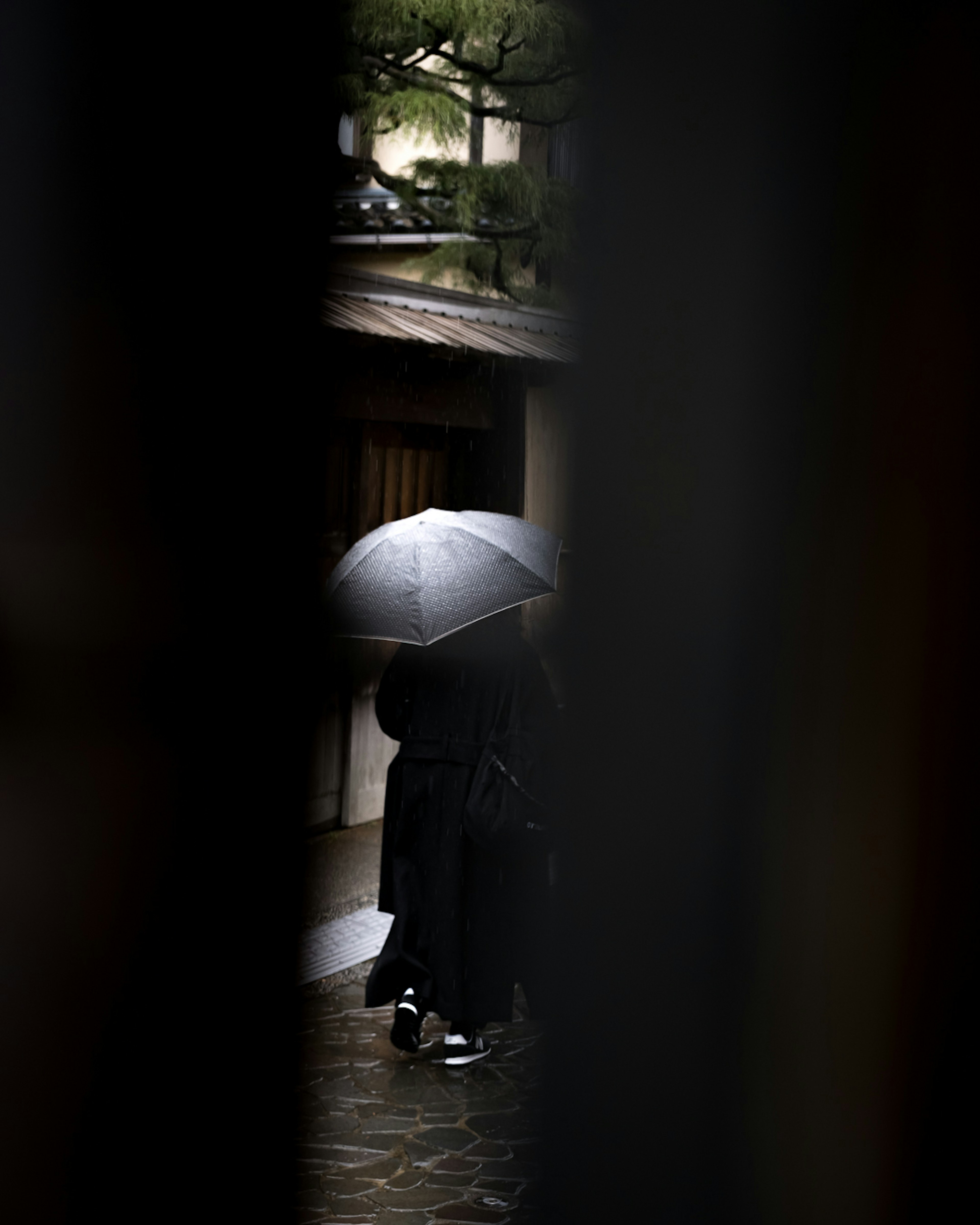 一个人在雨中走着，手里拿着黑色雨伞