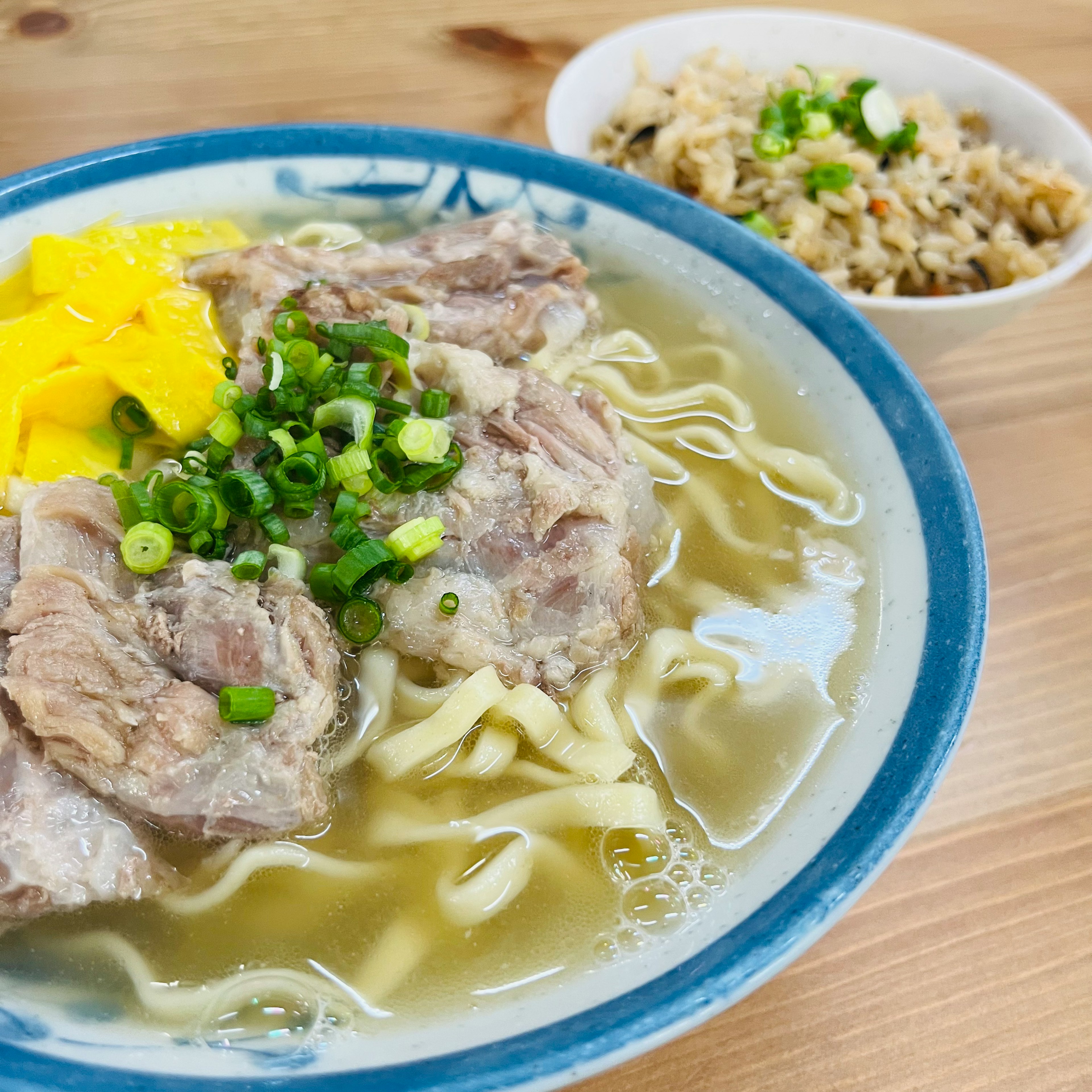 Un tazón de sopa con carne y fideos junto a un pequeño plato de arroz