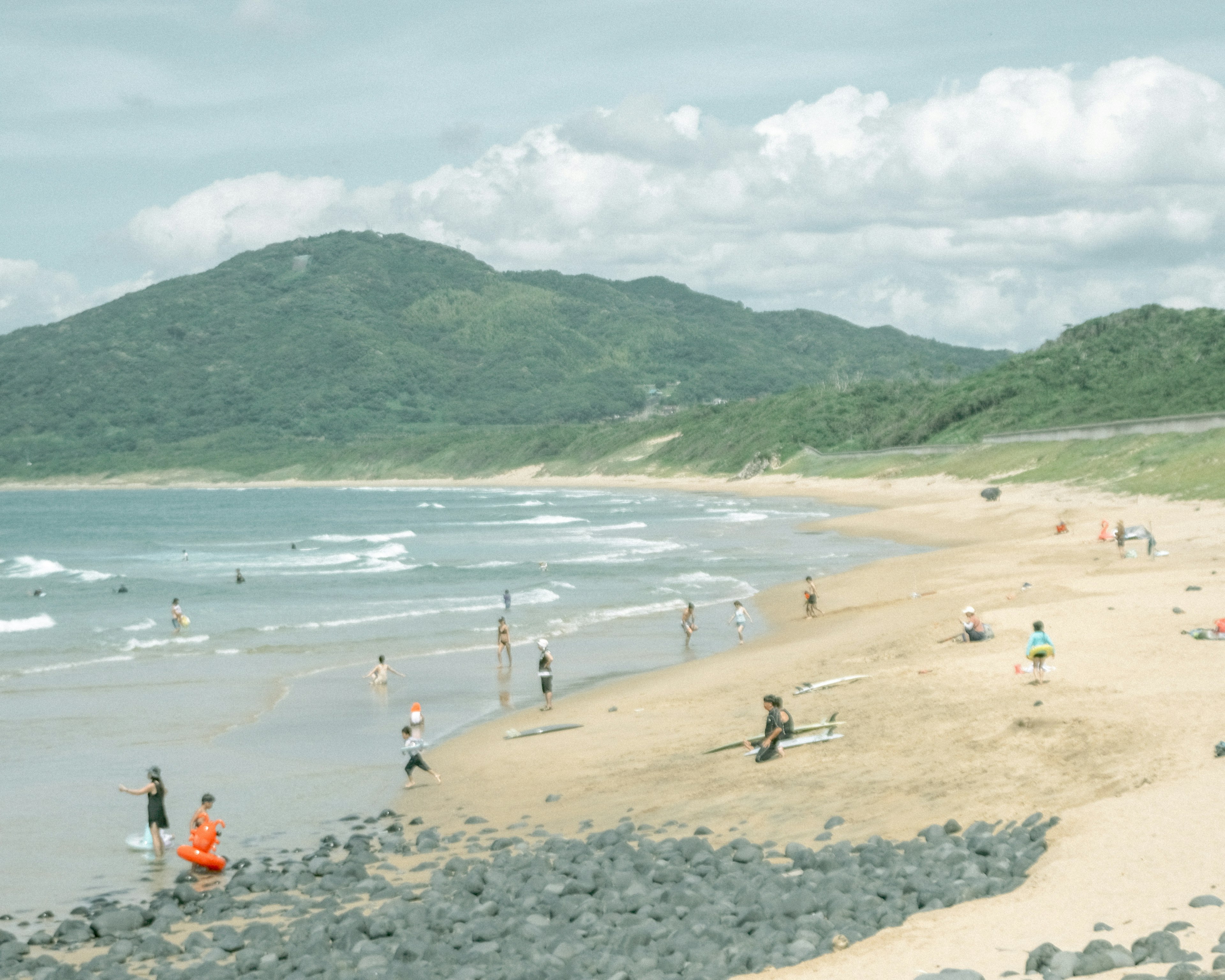 Escena de playa con personas disfrutando del agua y cielo nublado