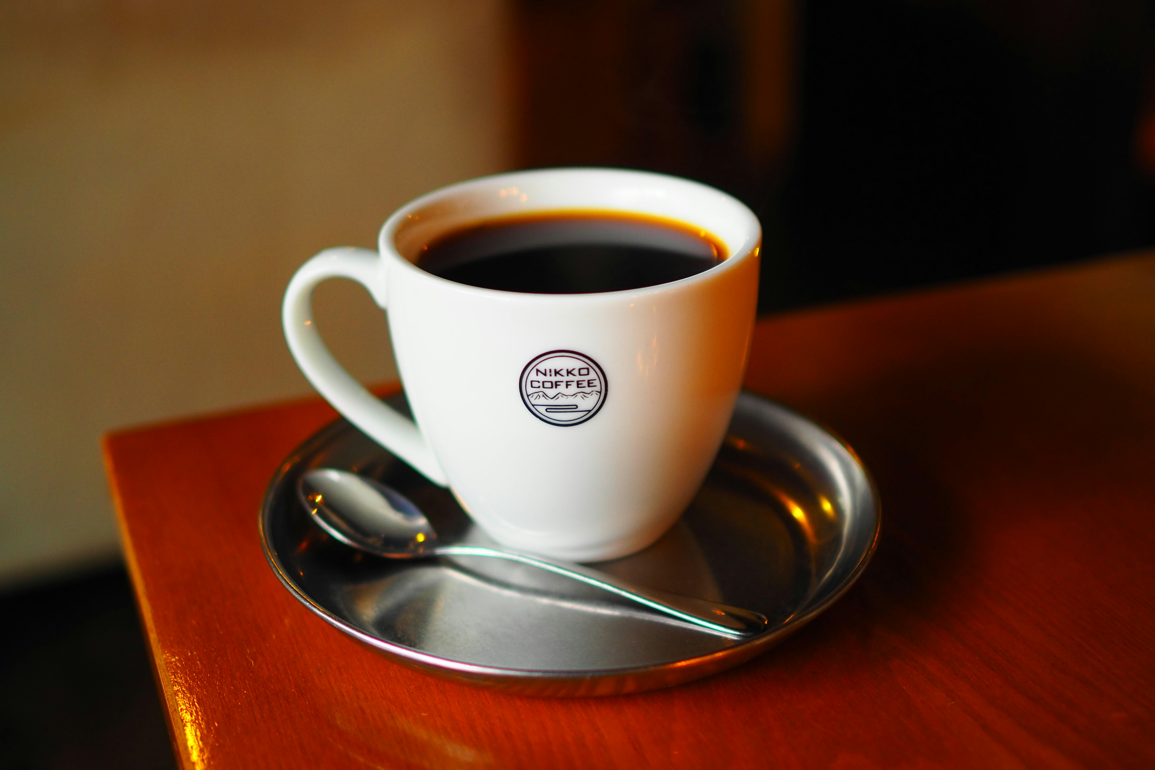 Une tasse à café blanche remplie de café noir sur une soucoupe en métal avec une cuillère