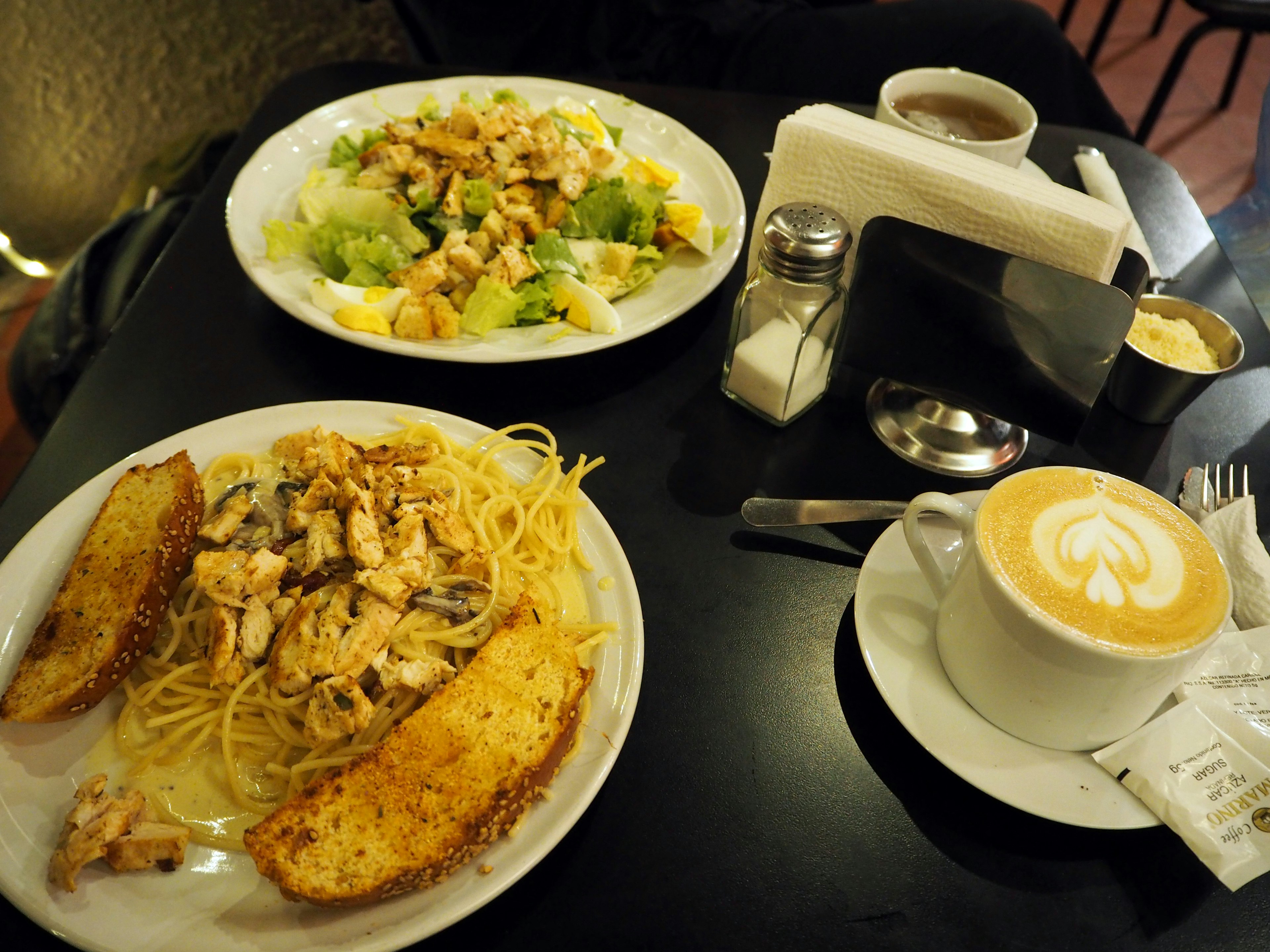 Teller mit Spaghetti und Hähnchen Salat und Kaffee auf einem Tisch