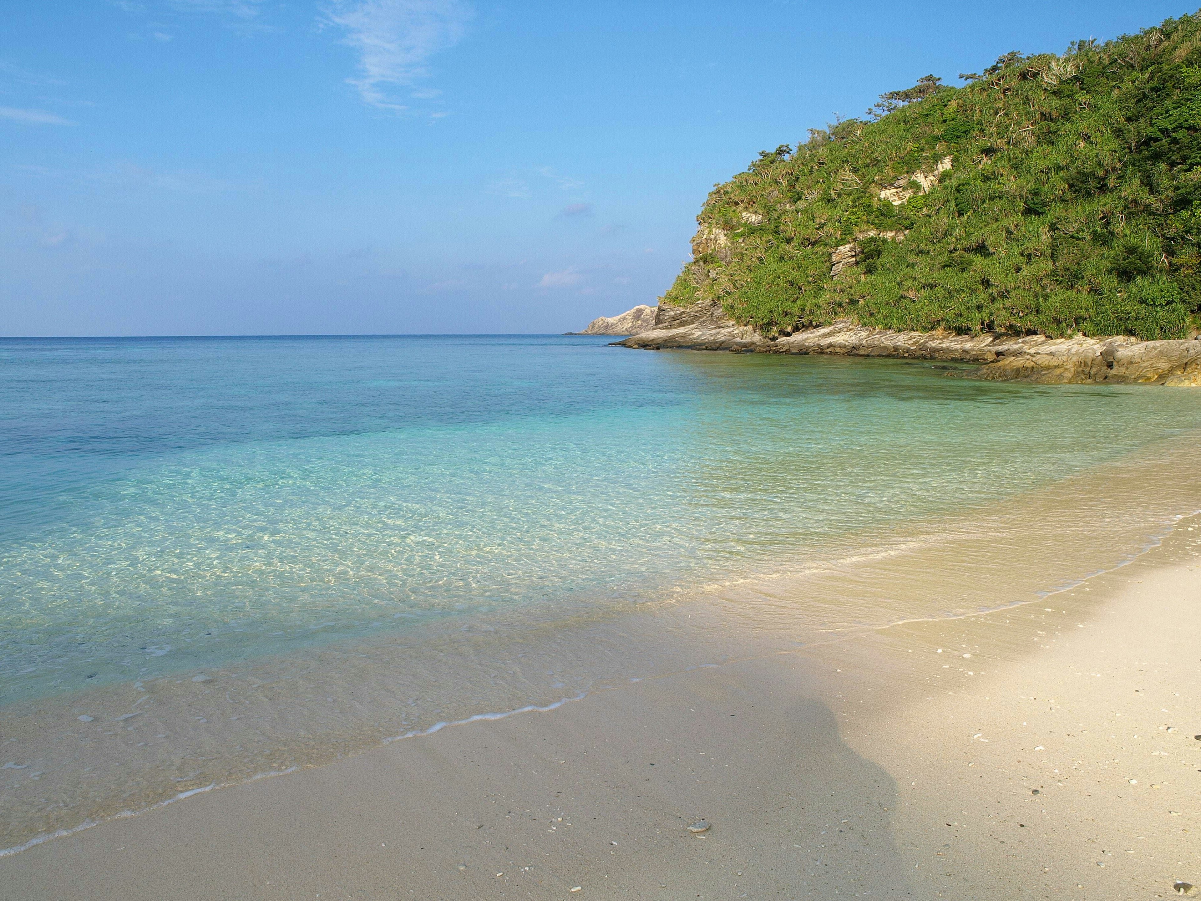 Pemandangan pantai yang tenang dengan air tenang dan langit biru Bukit hijau di latar belakang