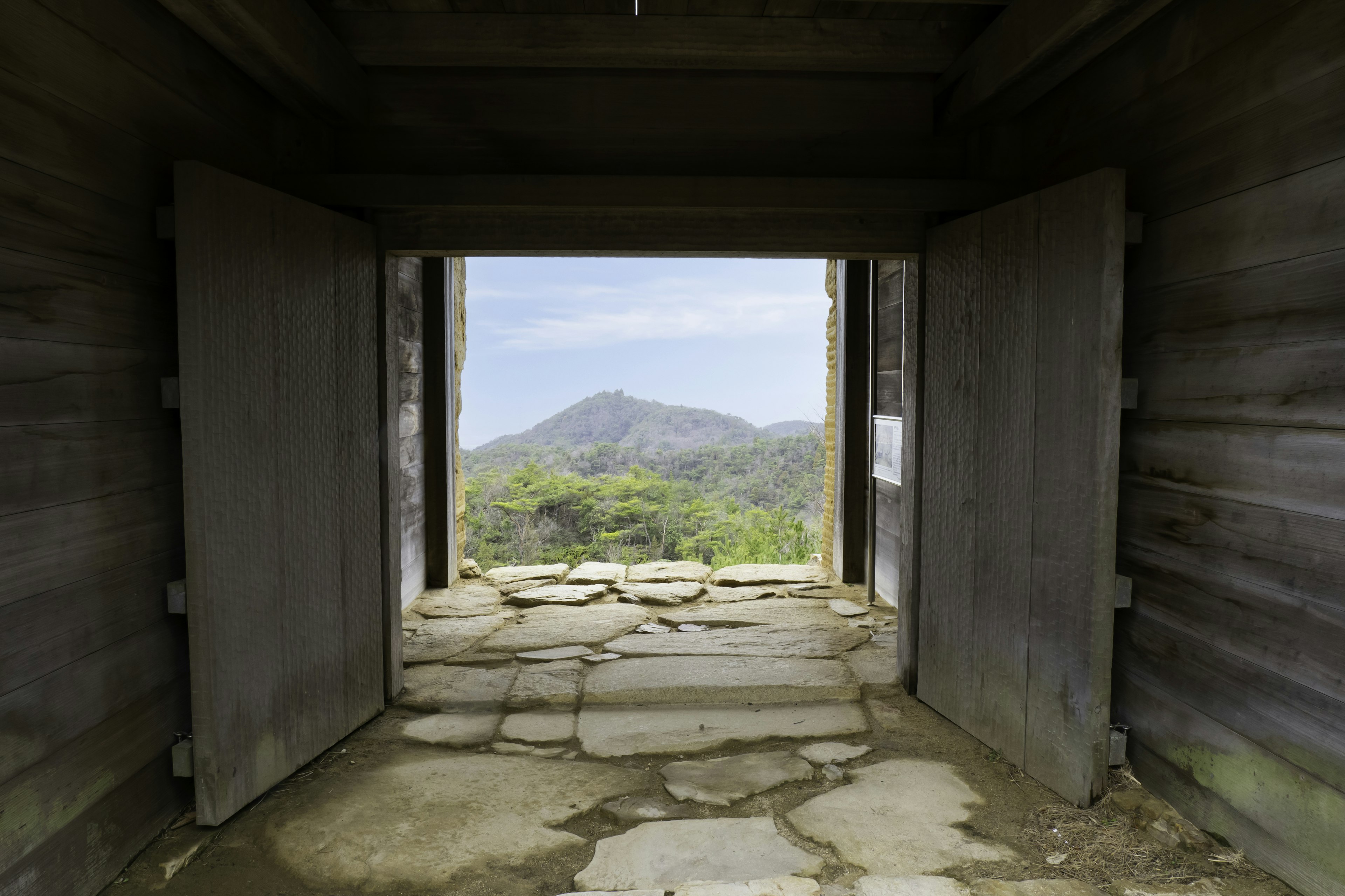 Interior of an old building with wooden doors revealing a mountain view