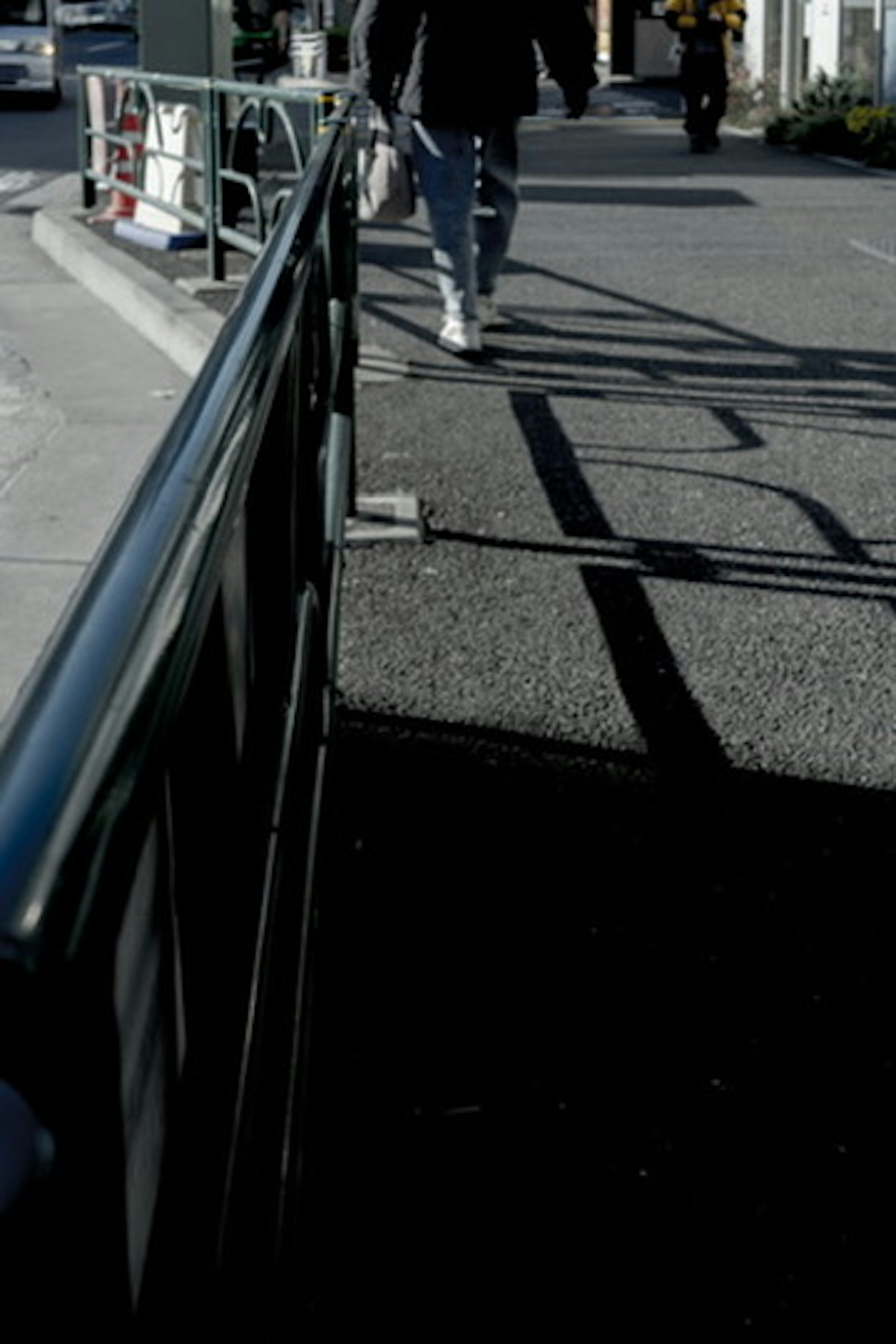 Une personne marchant près d'une rampe projetant des ombres sur le trottoir