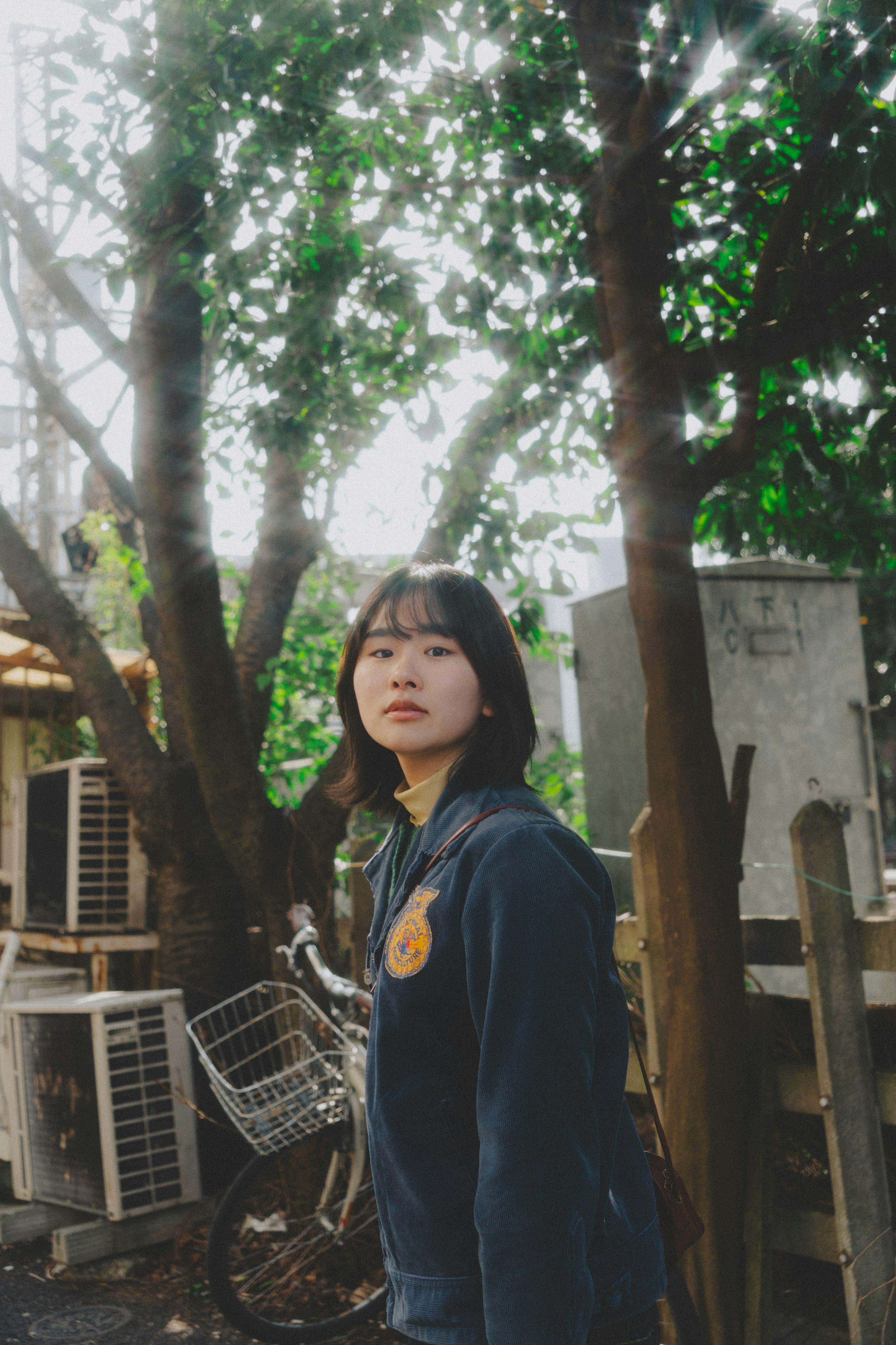 Portrait of a woman standing among green trees looking at the camera wearing dark clothing