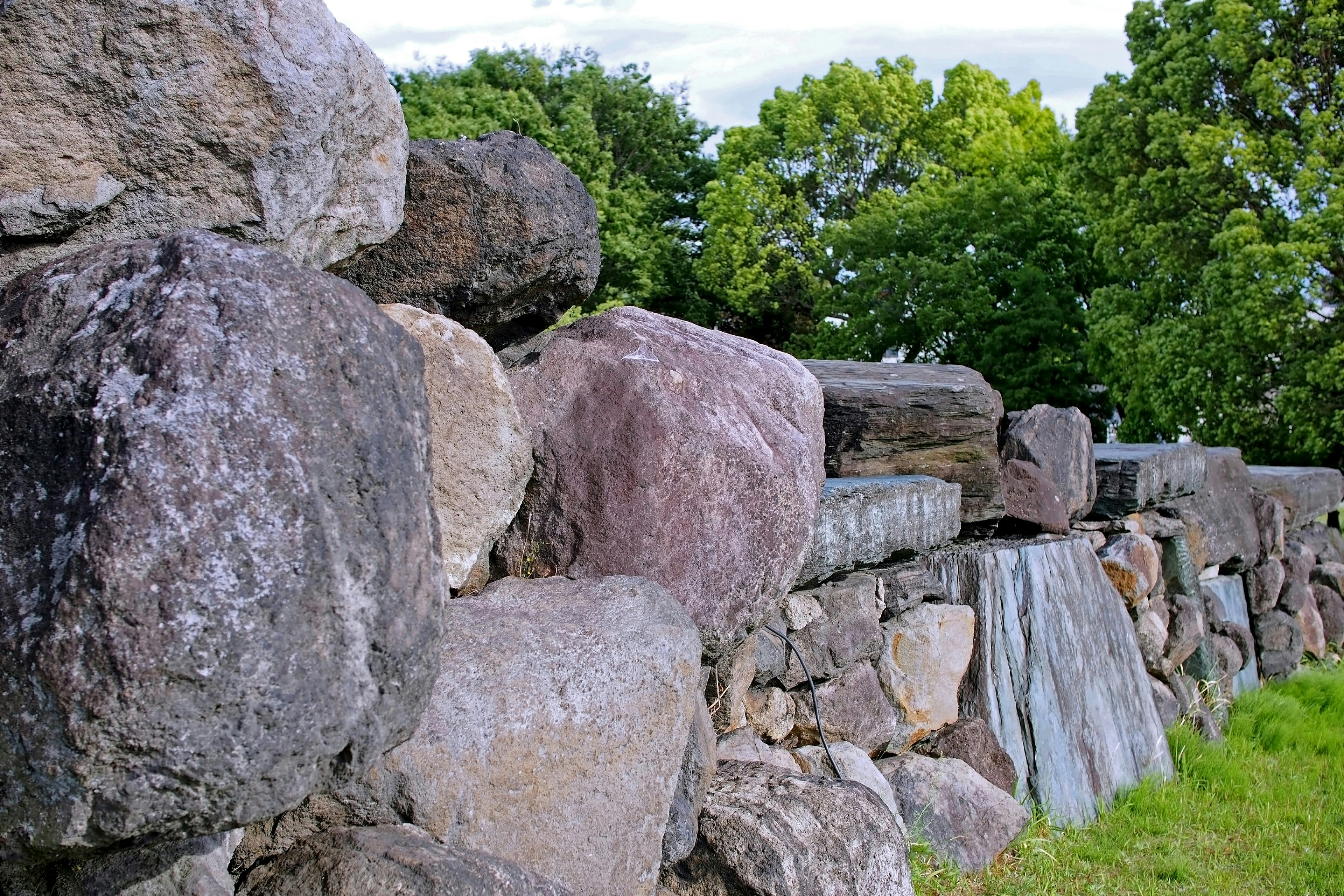 Close-up of a stone wall with large boulders and green trees in the background