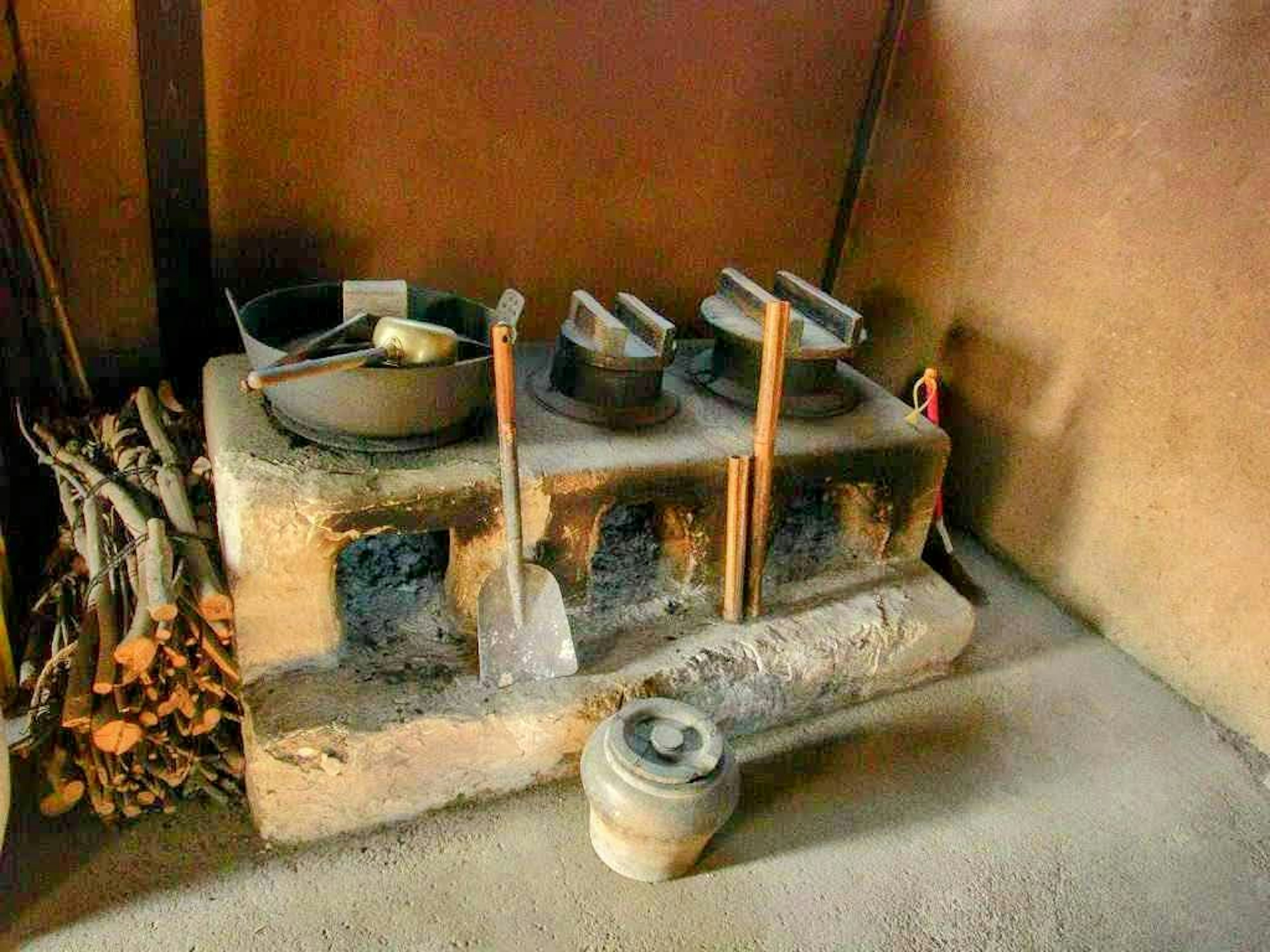 Ancienne cuisinière en terre avec ustensiles de cuisine et bois de chauffage