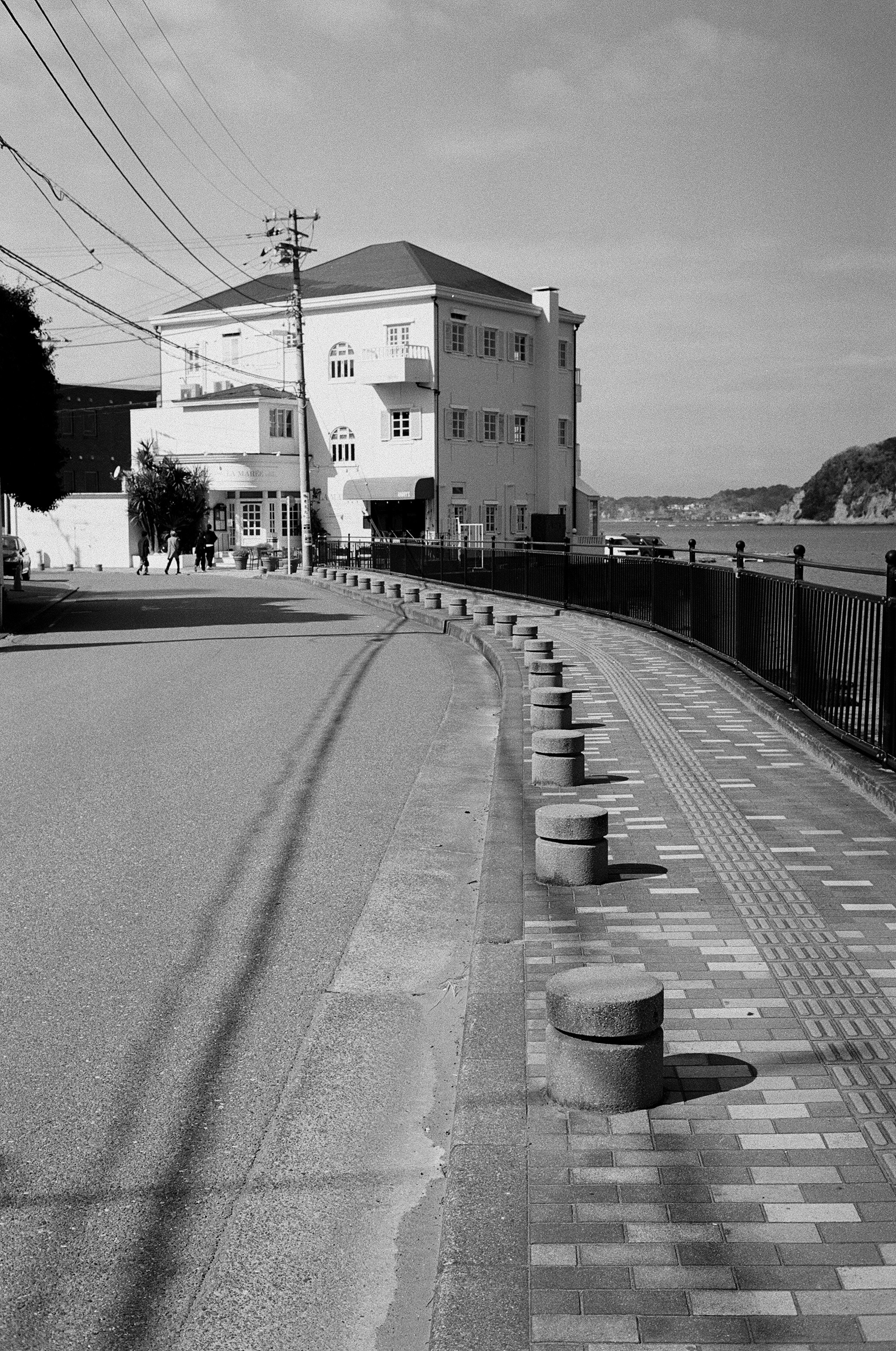 Escena callejera en blanco y negro con una carretera curva y una casa con bolardos redondos