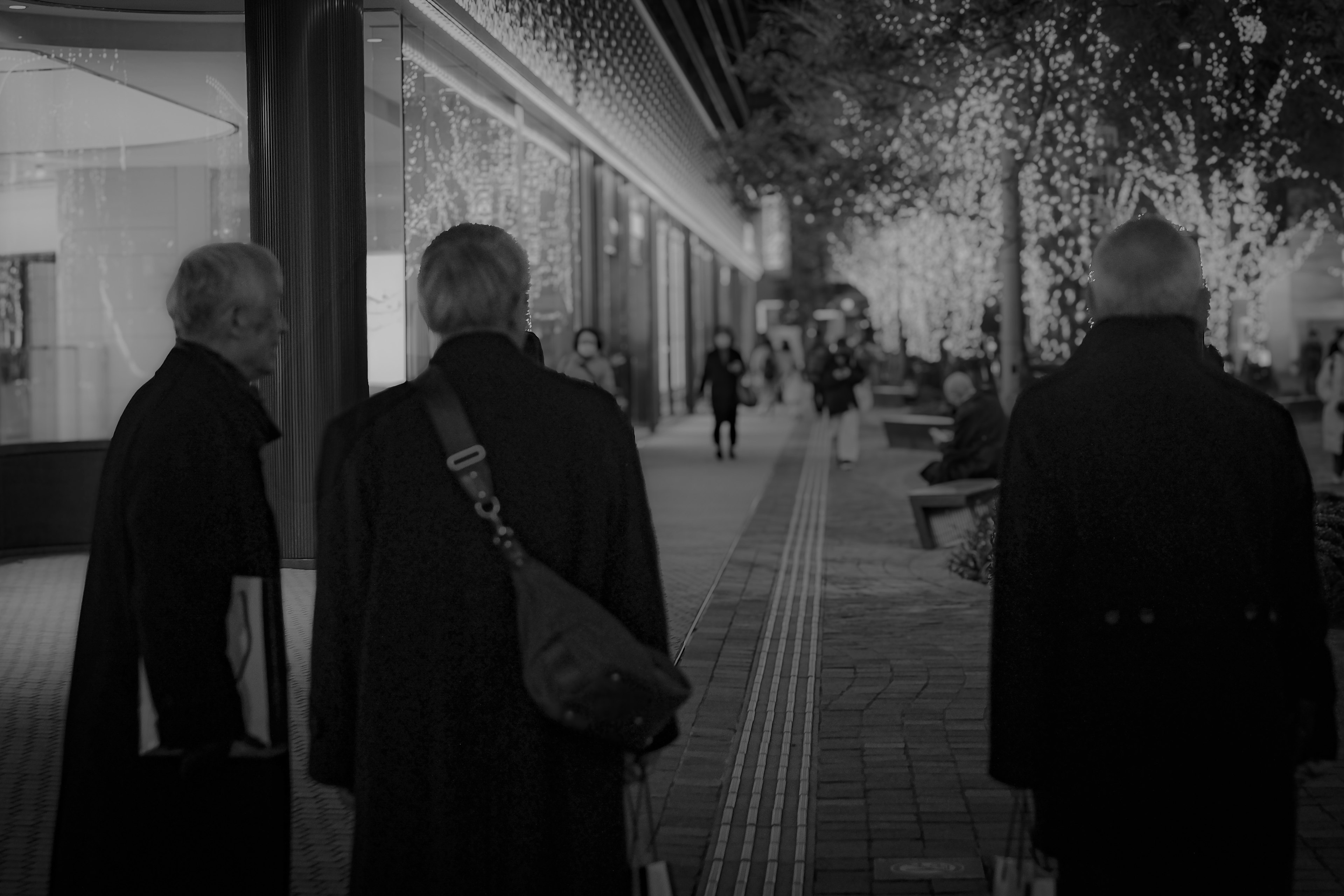 Tres hombres con abrigos negros caminando en una calle de la ciudad con luces