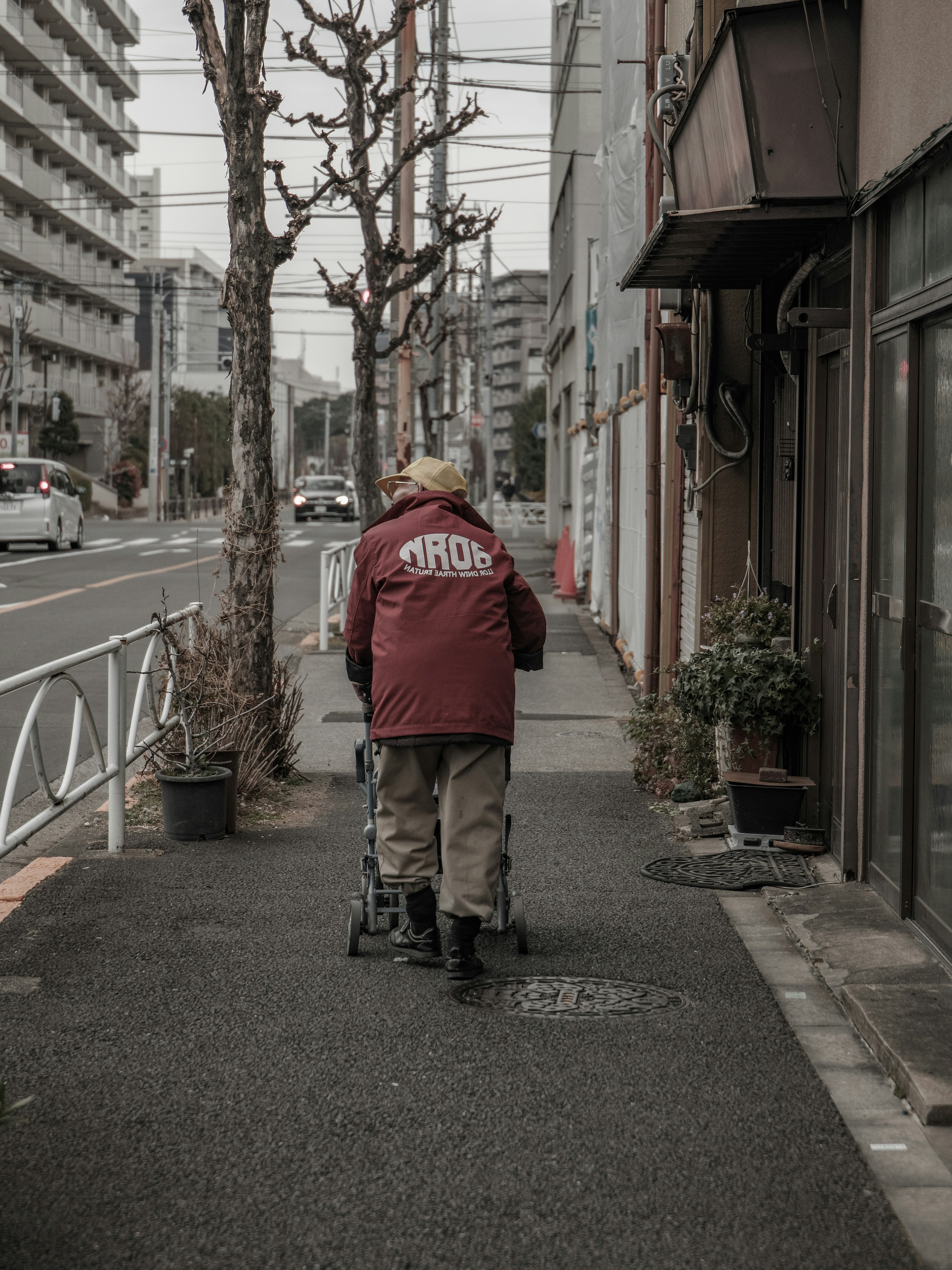 歩道を歩く高齢の男性 赤いジャケットと杖を持っている