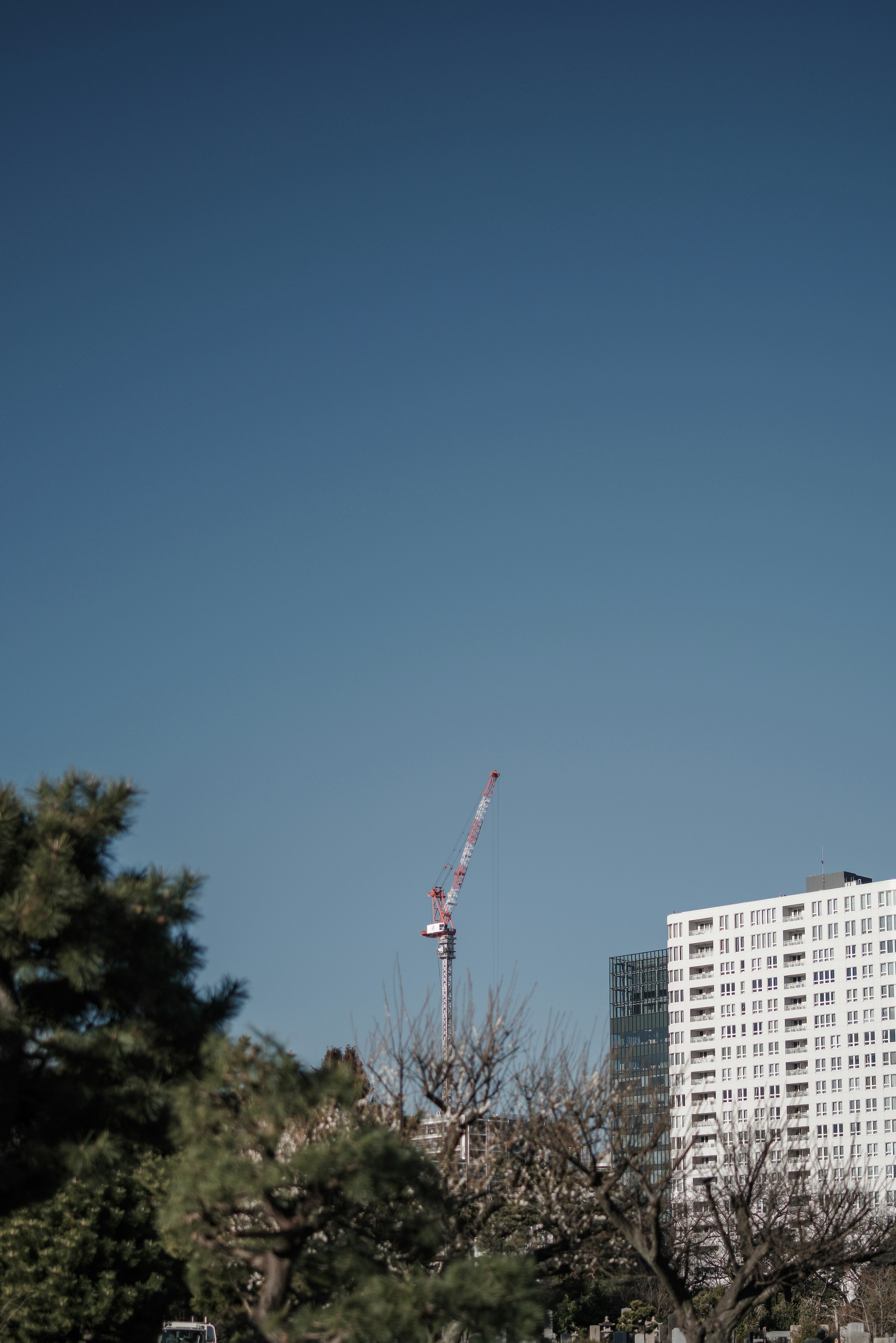 Construction crane against a clear blue sky with a high-rise building partially visible