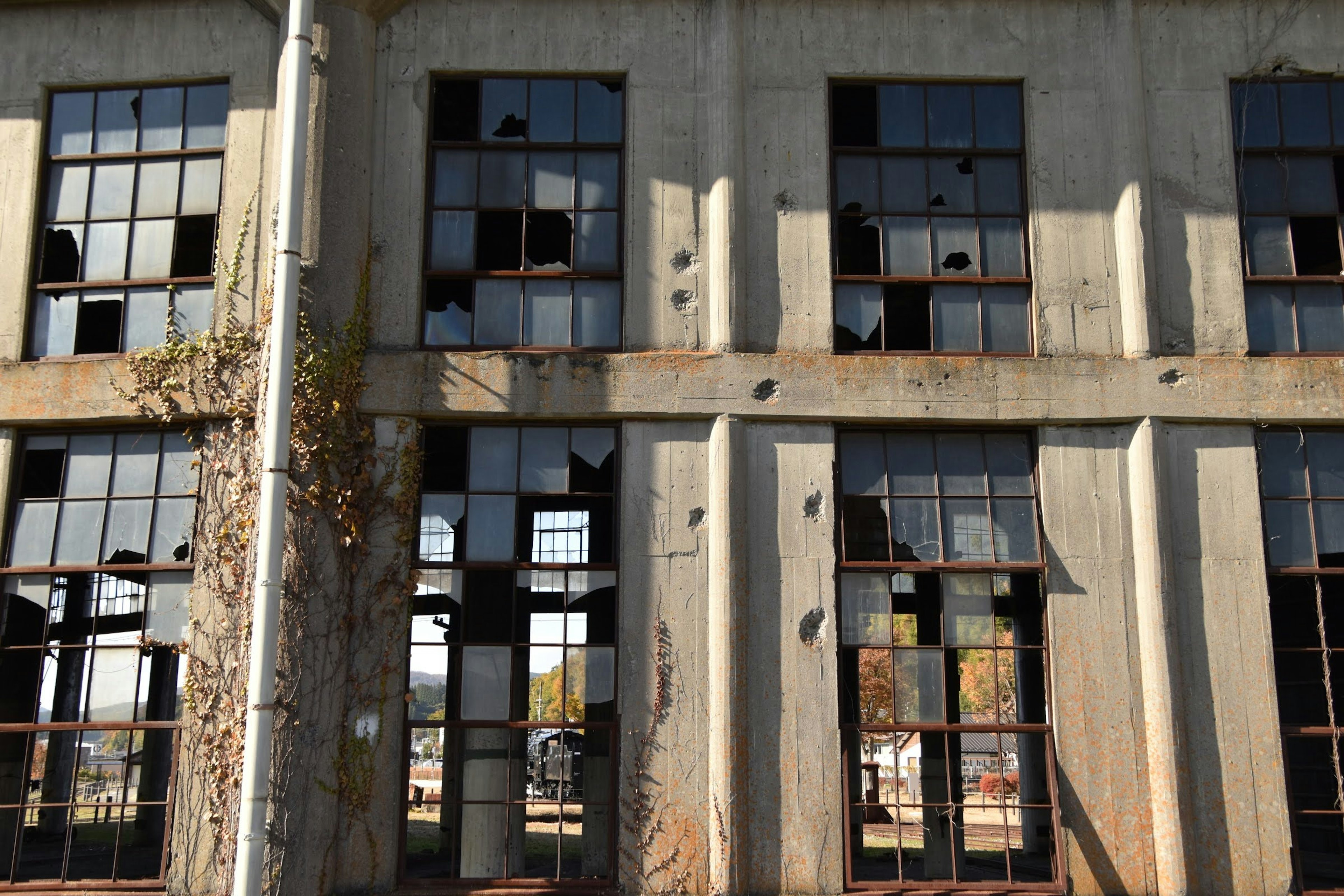 Exterior of an old industrial building featuring broken windows and concrete walls with a cracked surface