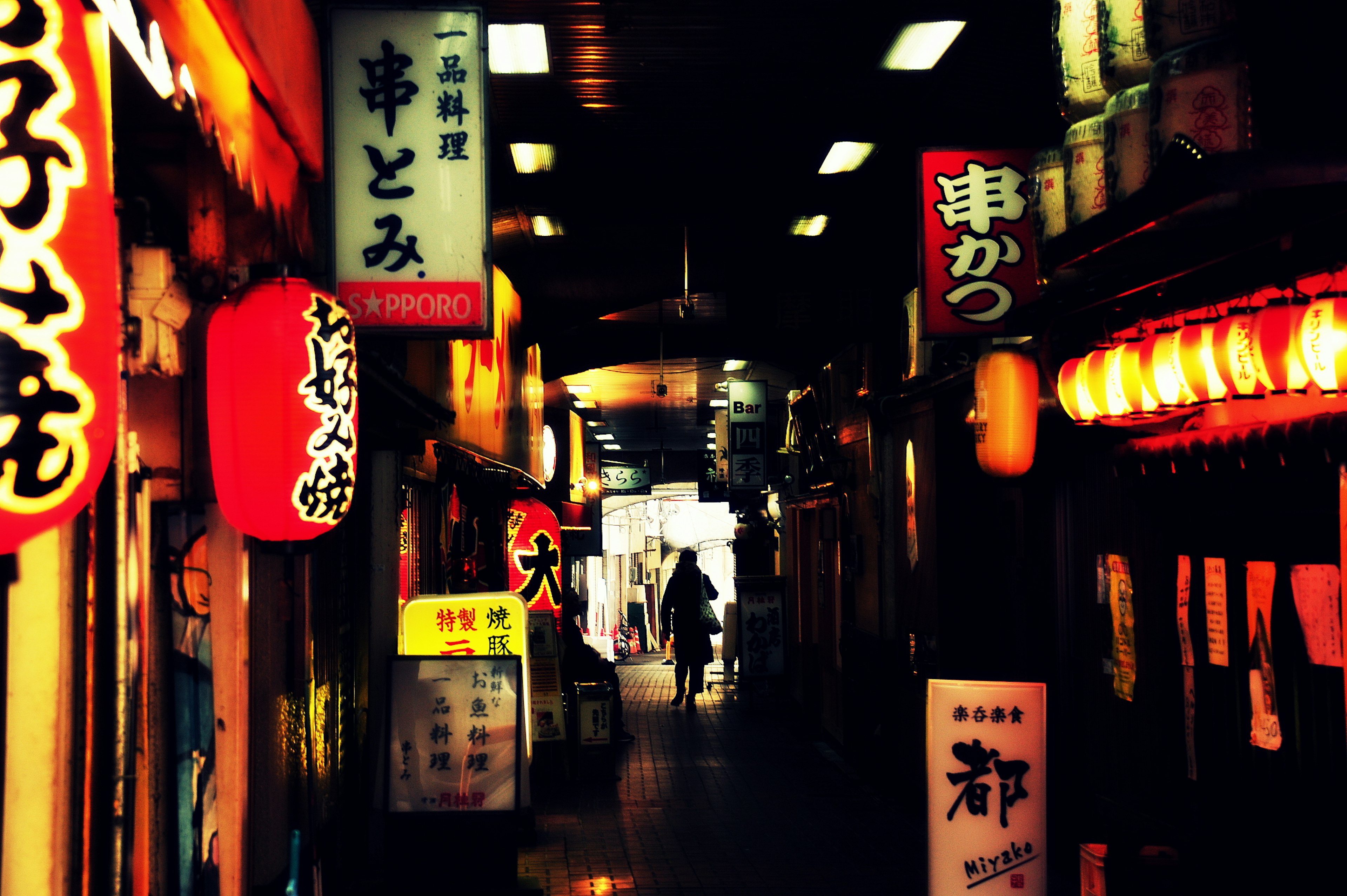 暗い路地に並ぶ飲食店の看板と提灯が光る風景