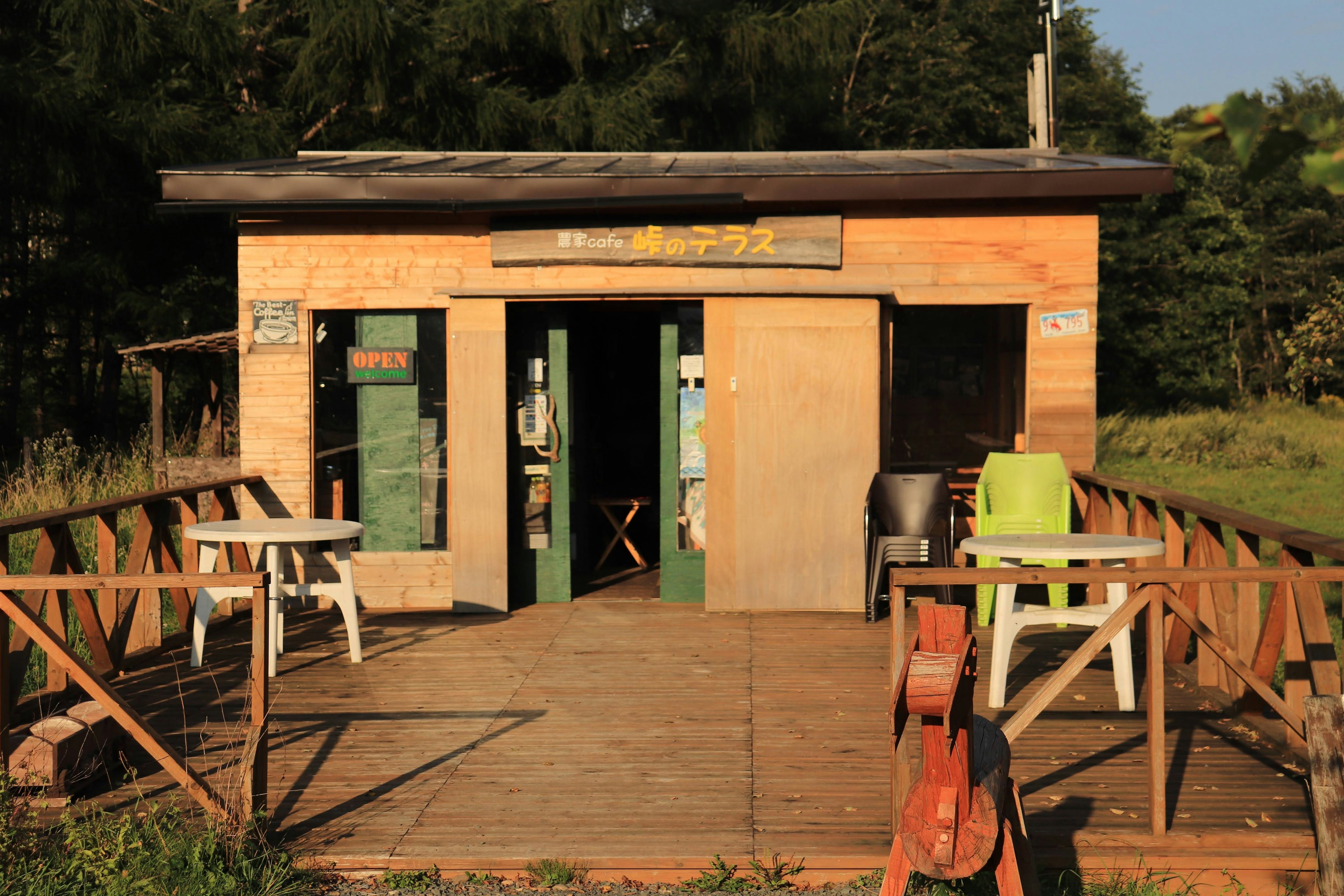 Cabane en bois entourée de nature avec des portes vertes et des tables extérieures