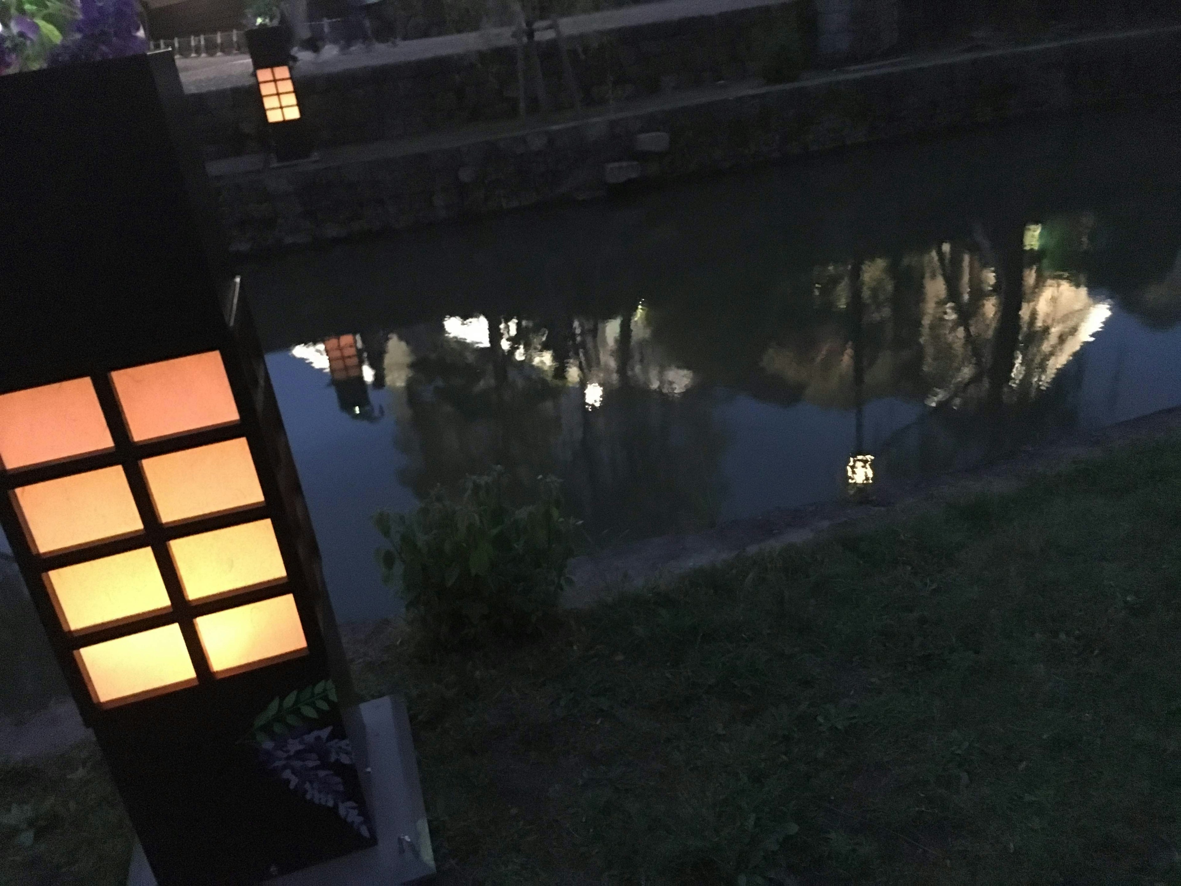 Eine Lampe beleuchtet den Flussufer bei Nacht, die sich im Wasser spiegelt