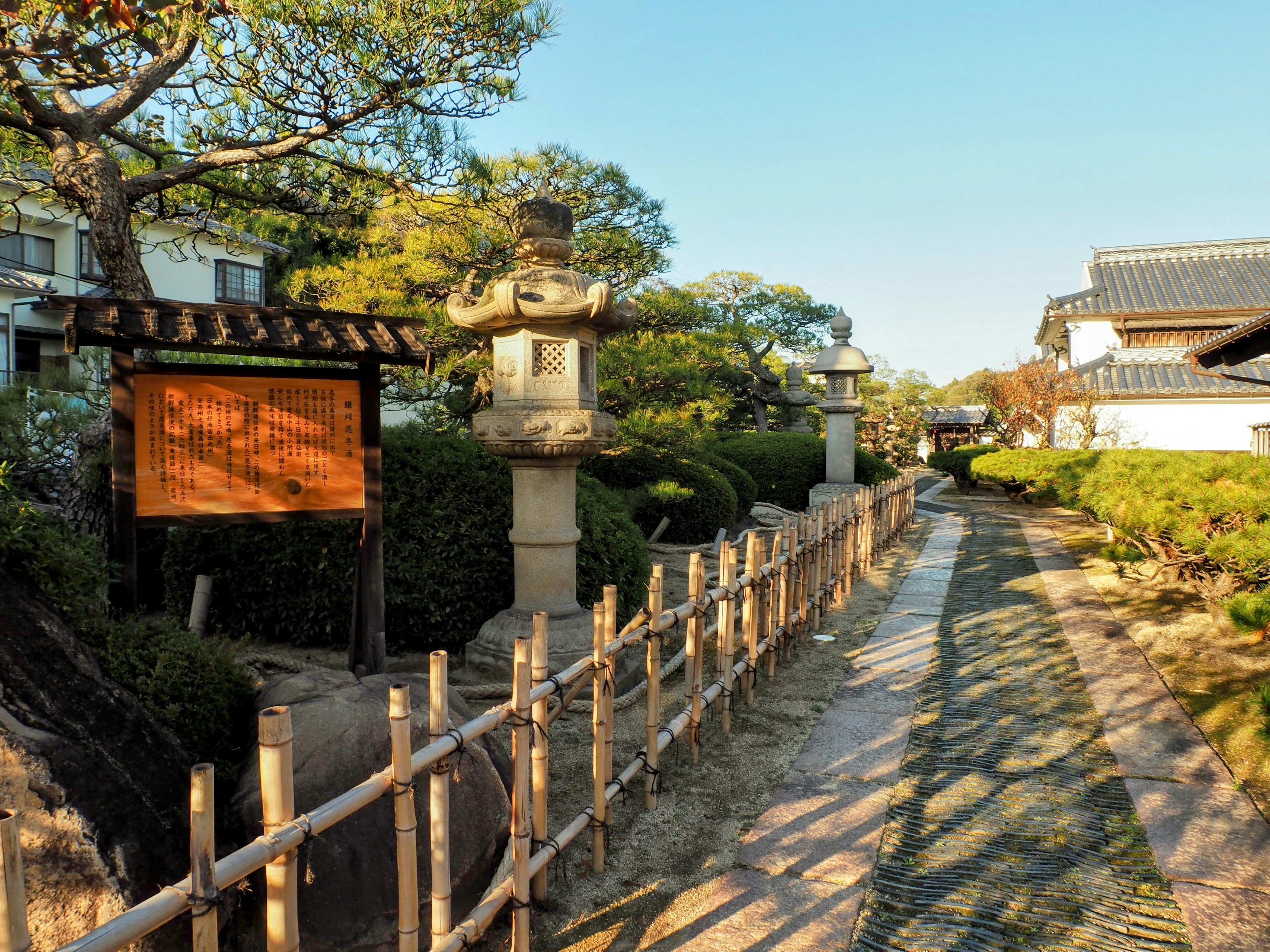 Scenic pathway in a tranquil garden featuring bamboo fence and stone lanterns