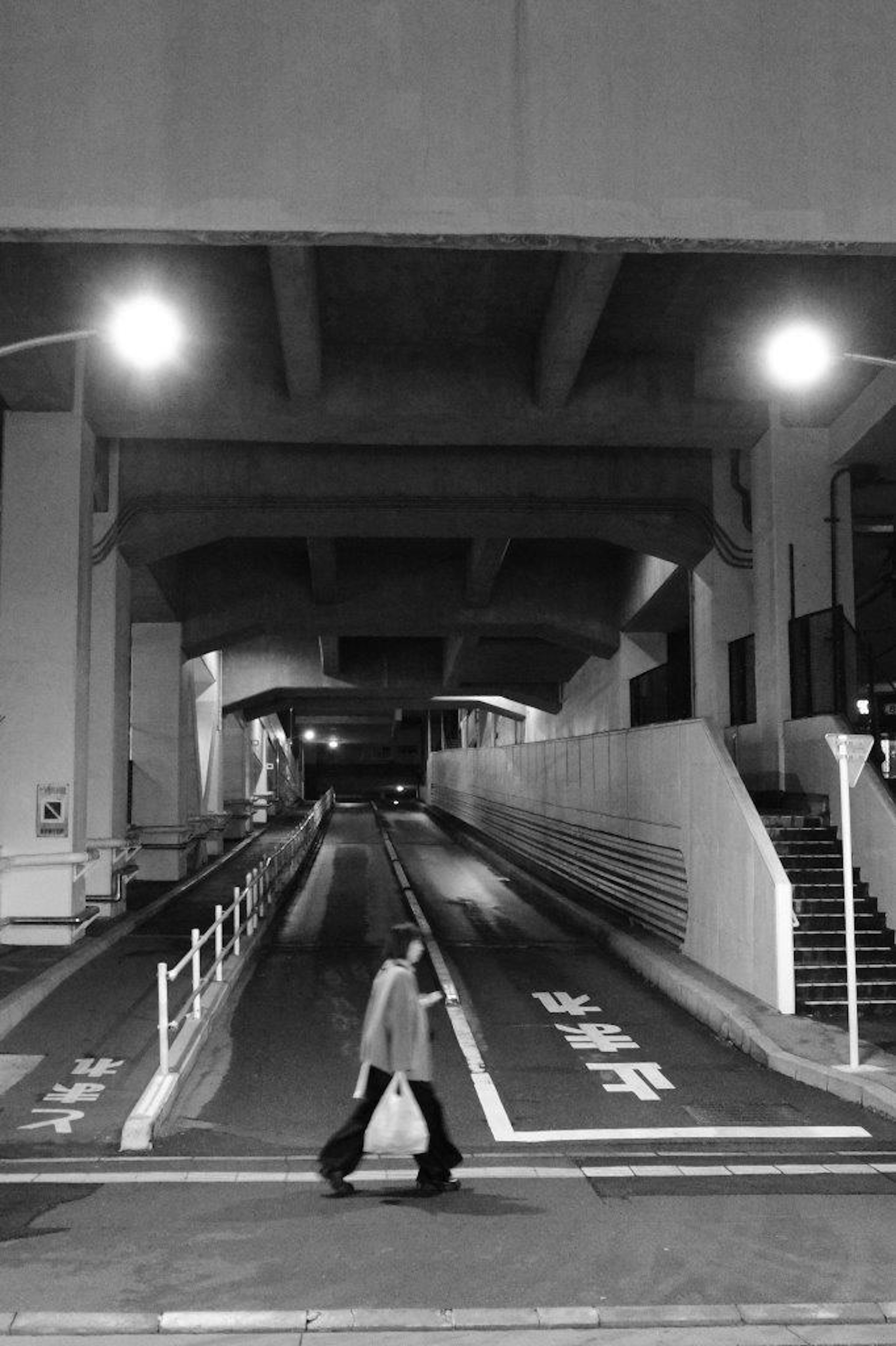 A person walking on a dimly lit street under a high bridge structure