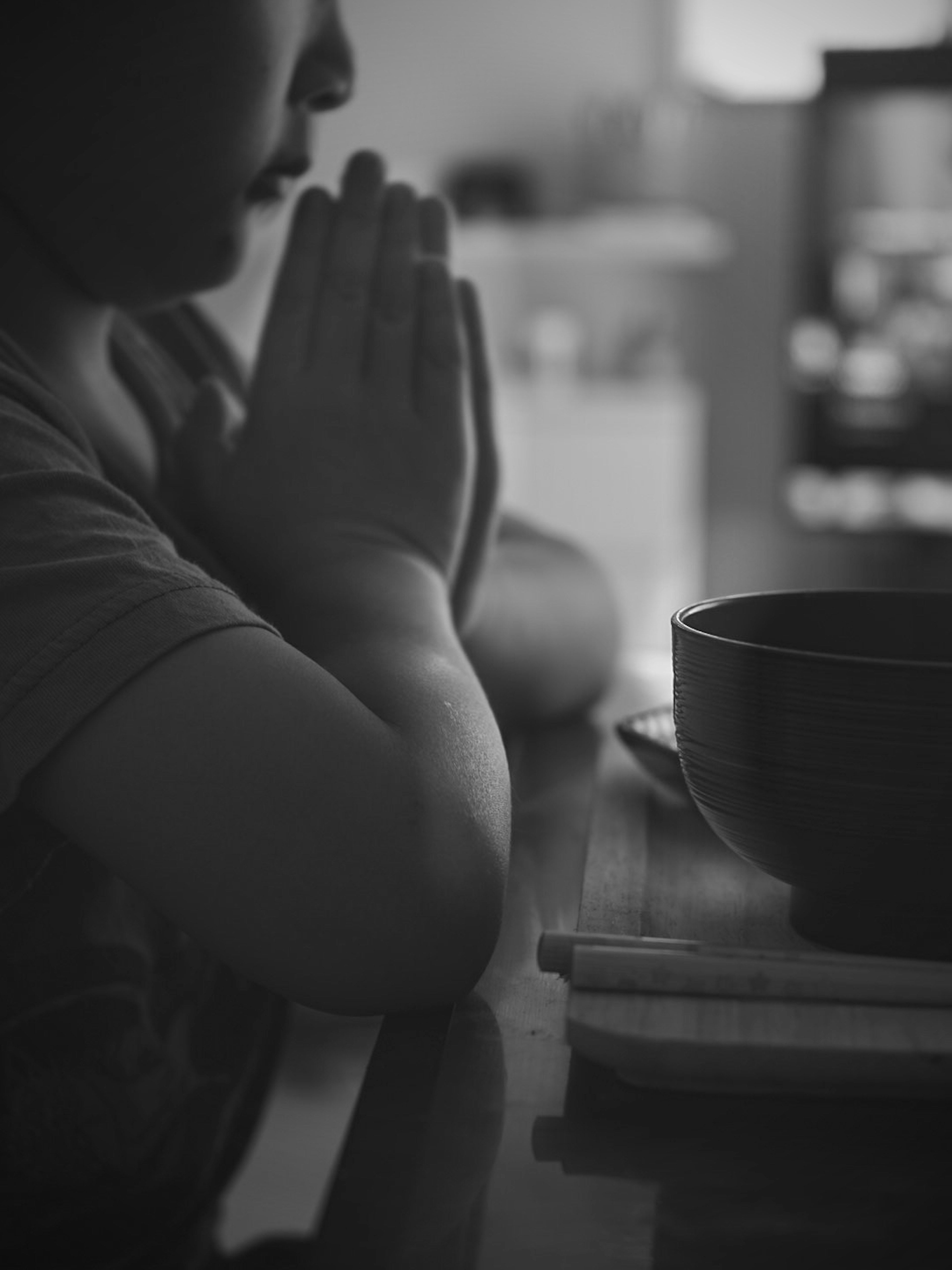 Child praying with hands clasped and a black bowl