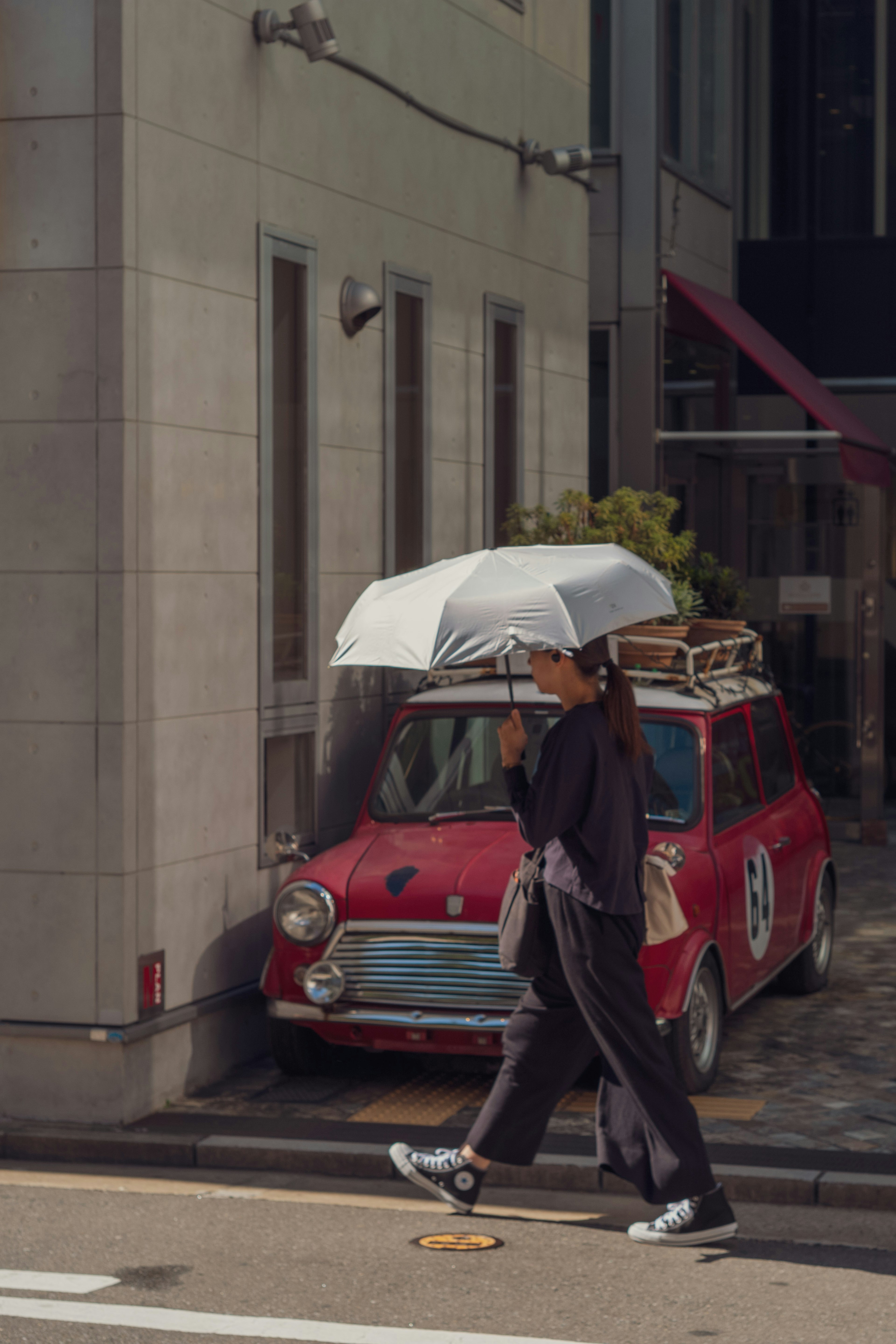 Una mujer caminando con un paraguas junto a un coche vintage rojo